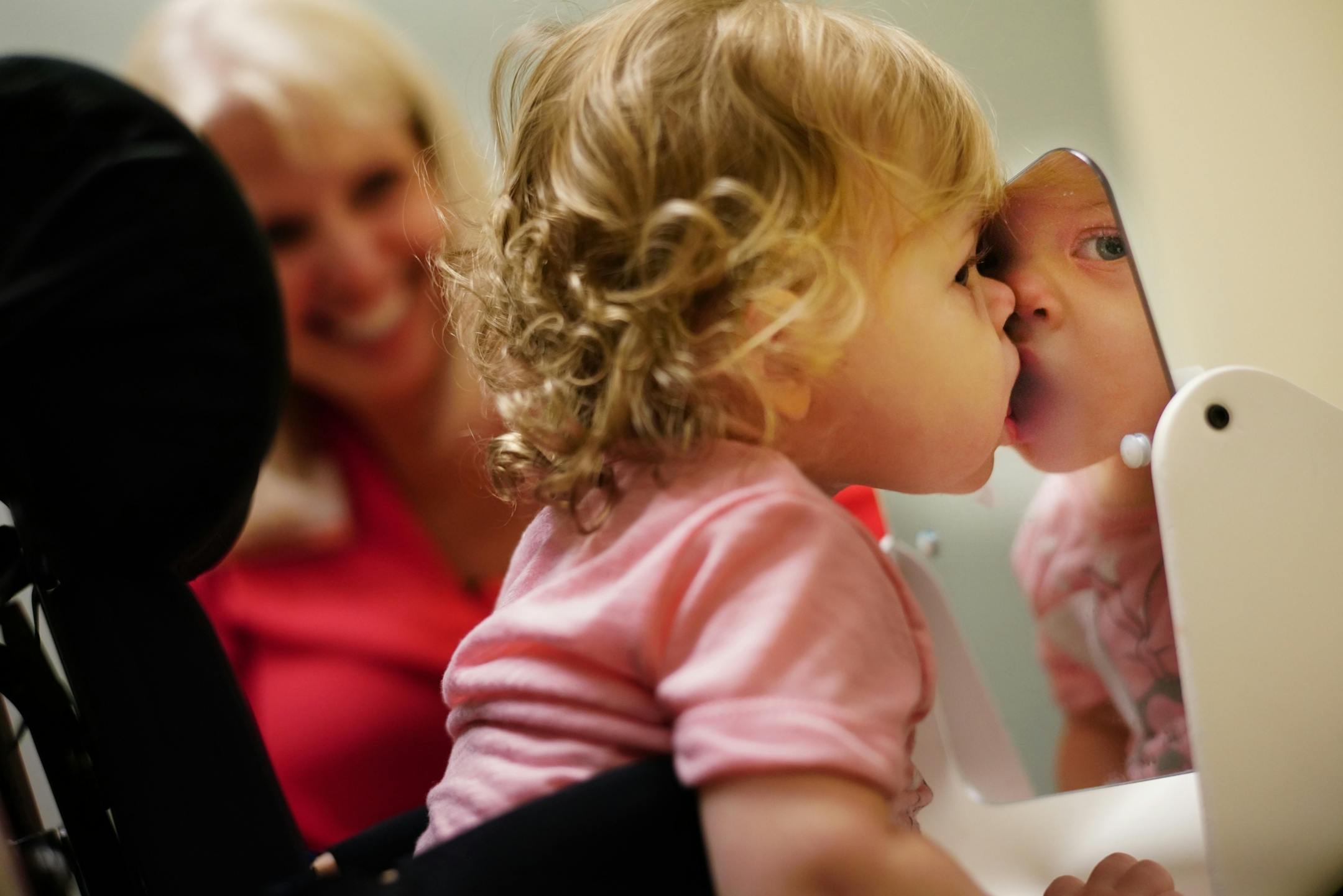 Speech therapist Susan Toavs uses toys with Aria to help her speech and overcome delays in growth caused by AFM. Aria enjoys seeing herself in the mirror. A benefit is that she is strengthening her core, which was weakened by AFM.