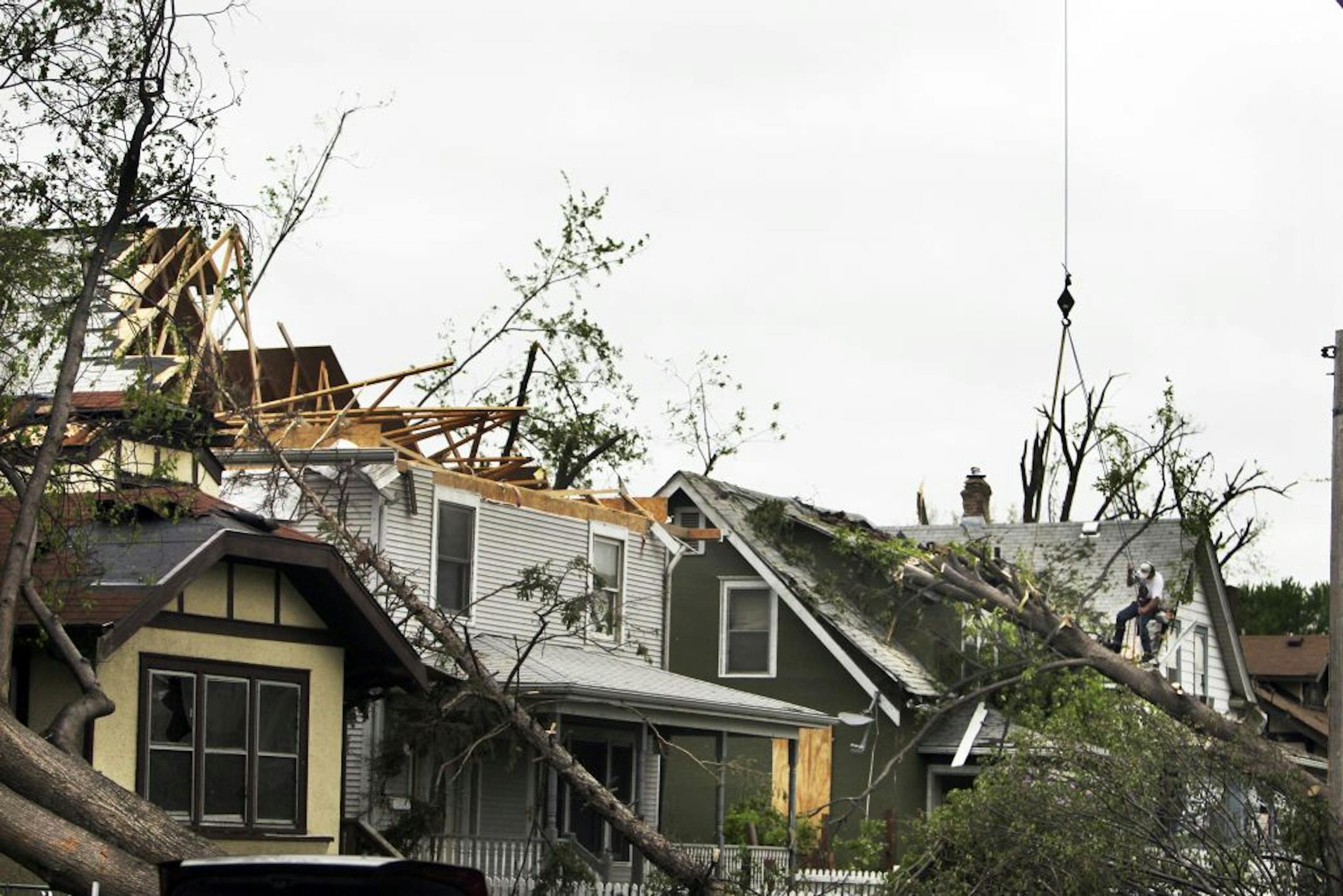 A worker from JCS Crane hooked up a line to a fallen tree before it was pulled off of a house in the 3000 block of Knox Av. N.