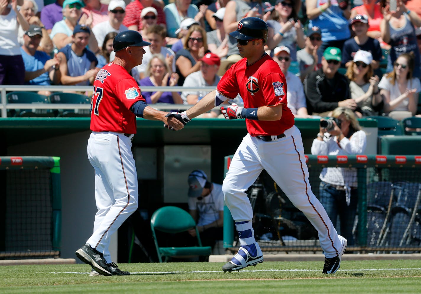 Minnesota Twins third base coach Mike Quade congratulates Joe Mauer on his two-run home run against the Baltimore Orioles during a spring training baseball game, Tuesday, March 22, 2016, in Fort Myers, Fla. (AP Photo/Tony Gutierrez)