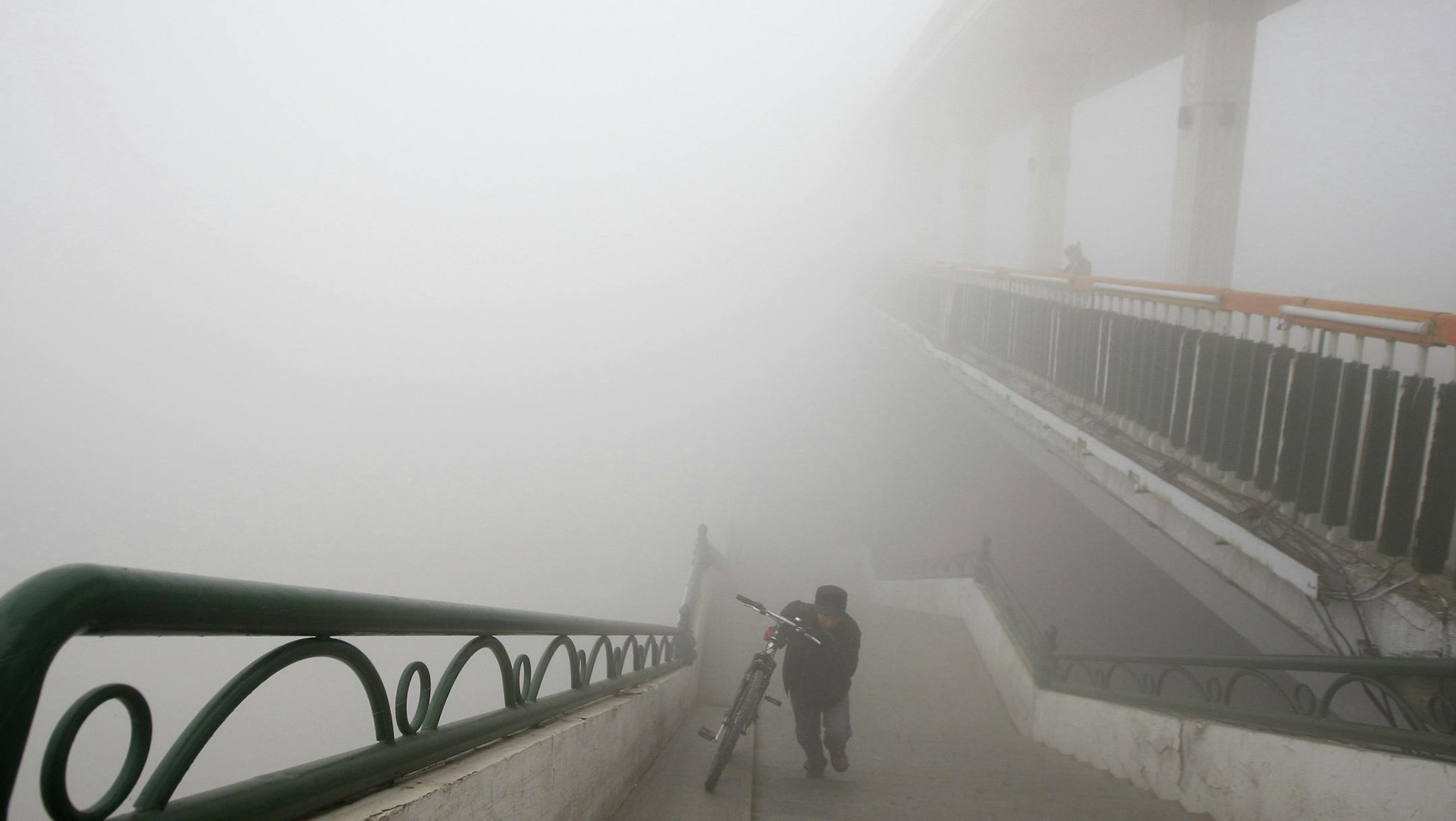 A man pushes a bike onto a bridge during a day of heavy pollution in Harbin in northeast China's Heilongjiang province Monday Oct. 21, 2013. Visibility shrank to less than half a football field and small-particle pollution soared to a record 40 times higher than an international safety standard in the northern Chinese city as the region entered its high-smog season. (AP Photo) CHINA OUT ORG XMIT: MIN2013110115382250