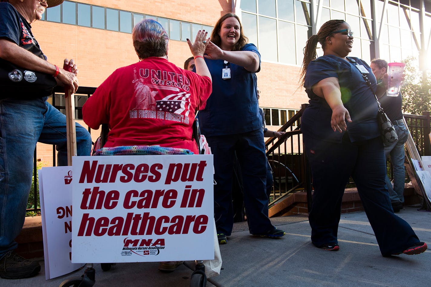 Mary Sansom, left, high-fives nurse Tina Kriech as she exits United Hospital at 7 a.m. and past a growing picket line.