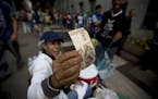 A street vendor inspects the authenticity of a 100-bolivar note as people stand in line outside a bank to deposit their bank 100-bolivar bank notes, i