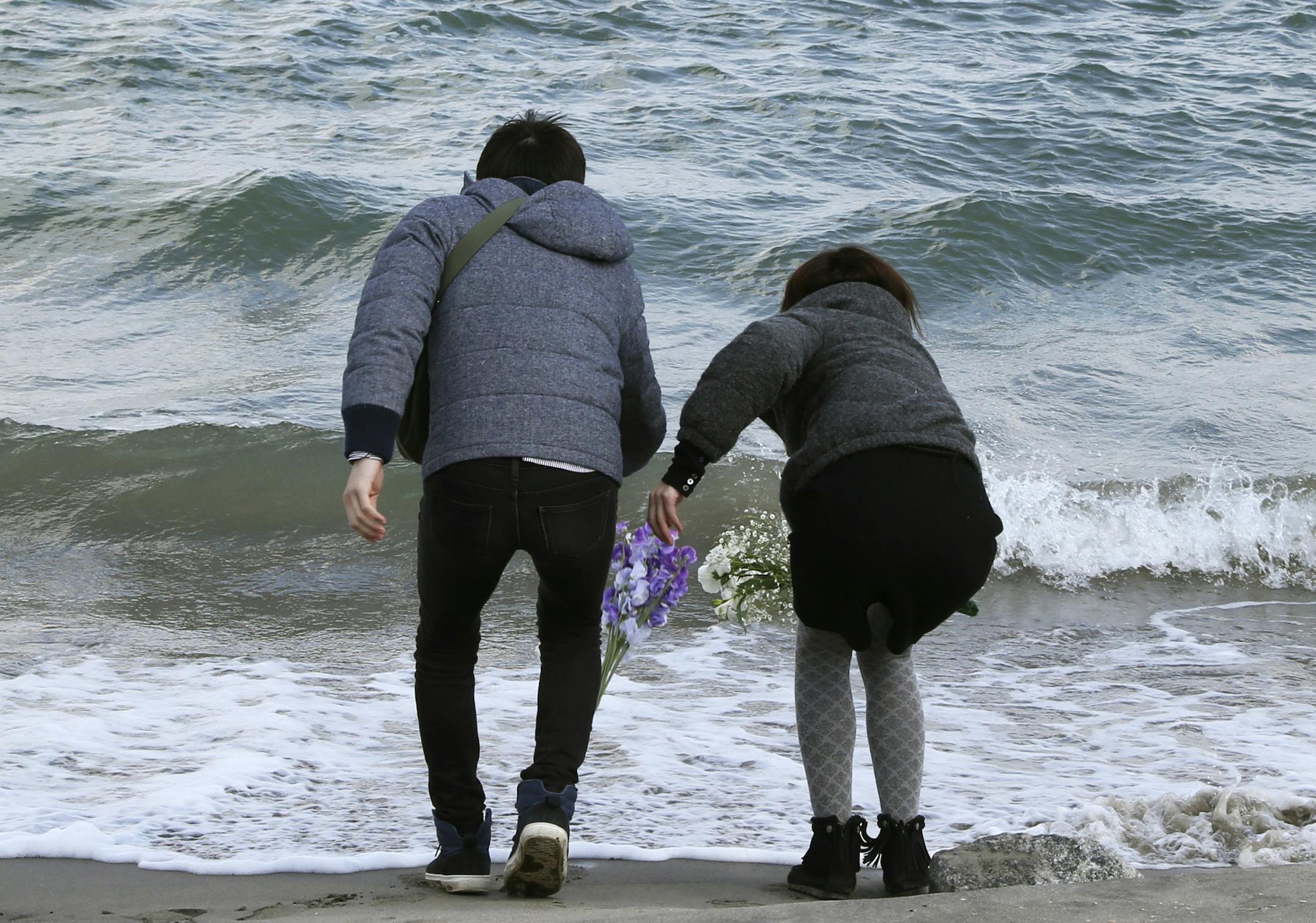 Employees of a nursing home Tsutomu Sato, 34, left, and Yoko Katayama, 30, toss bouquets of flowers into the sea in remembrance of the 36 people who died in the home during the March 11, 2011 earthquake and tsunami in Minamisoma Fukushima Prefecture, northeastern Japan, Tuesday, March 11 2014. Japan on Tuesday marks the third anniversary of the March 11, 2011 earthquake and tsunami that killed 15,884 people and left more than 2,600 unaccounted for in vast areas of its northern coast. (AP Photo/K