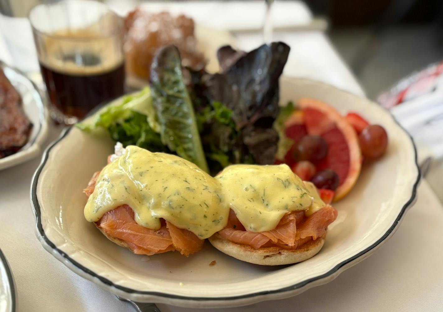 Two eggs benedict with dill-flecked hollindaise over smoked salmon on english muffins. There's also a salad of fresh greens. on the plate and fresh fruit.