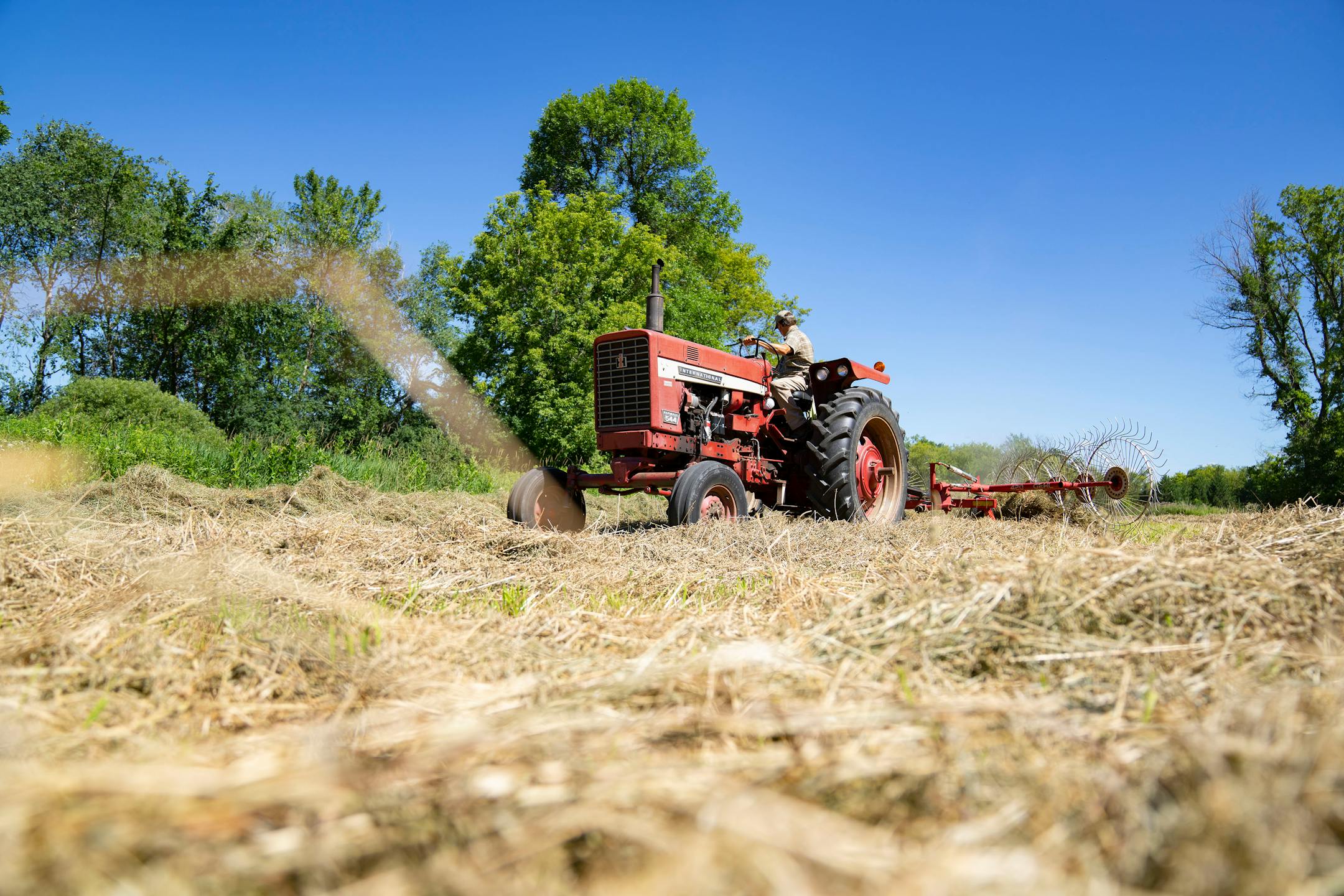 Max Gustafson rakes hay with his tractor Thursday, July 21, 2022 on rented land near his farm in Center City.