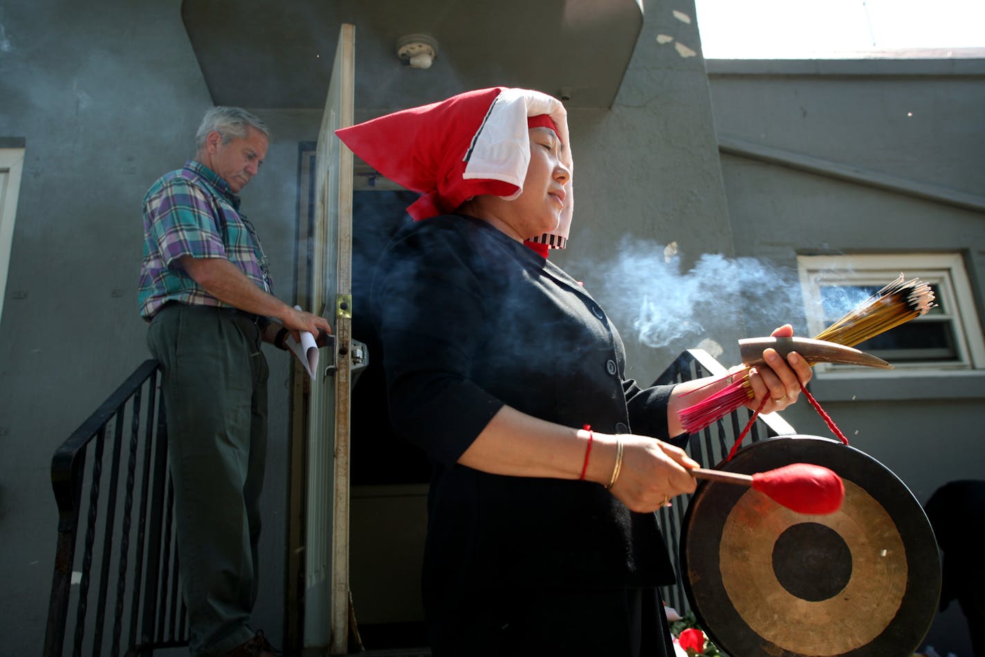 Hmong shaman Mai Yang, of Maplewood, began a ceremony to communicate with spirits inside the Hmong Funeral Home. She struck a gong to persuade them to leave the building because it will soon be demolished. Craig O'Brien of the Office of Planning and Economic Development is behind her.