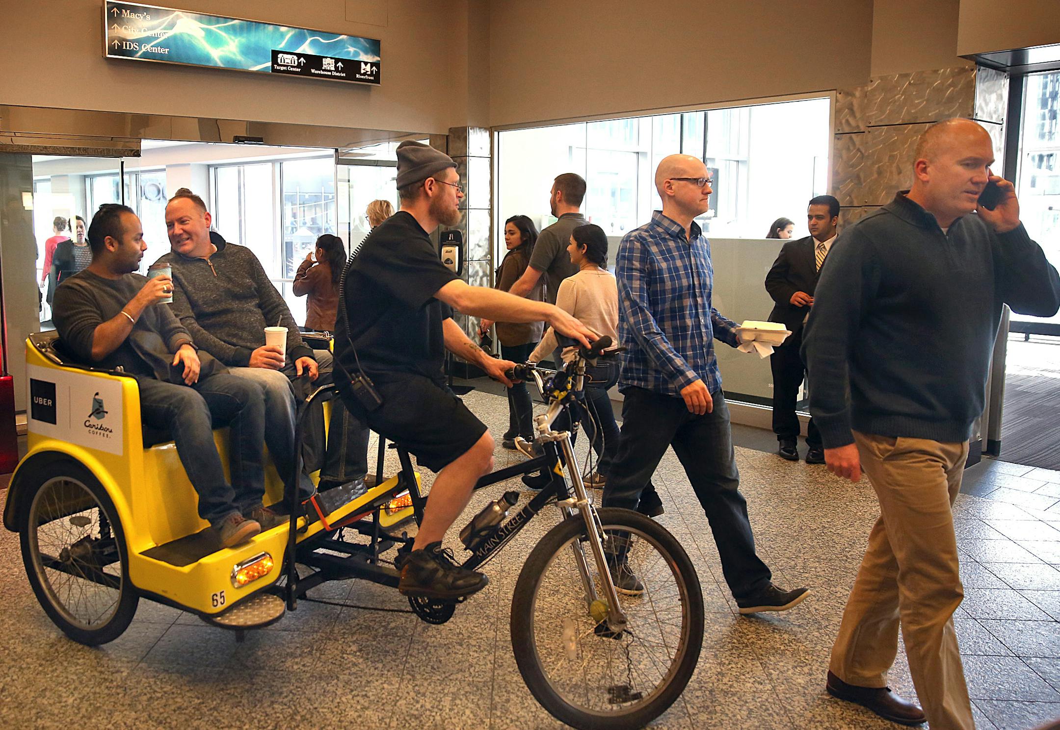 Pedicab driver Shawn Schoeder looked for a opening in foot traffic in the skyway, while passengers Nishant Gupta (left) and Bill Volkmeier, both Minneapolis, enjoyed the ride. Uber and Caribou Coffee teamed up to offer free rides in the skyway Friday.