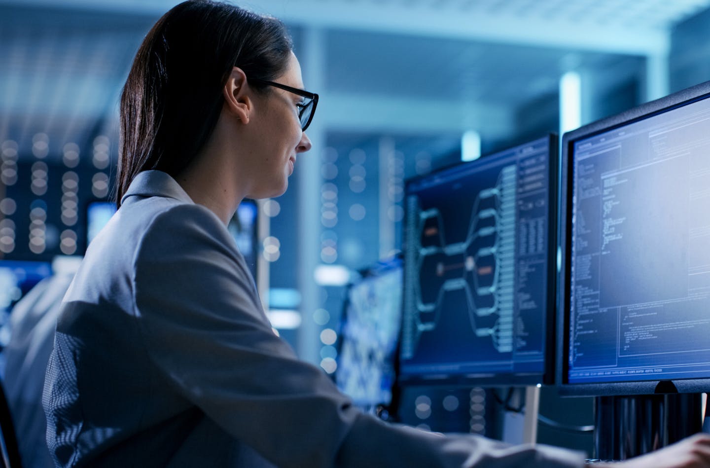 Close-up Shot of Female IT Engineer Working in Monitoring Room. She Works with Multiple Displays.