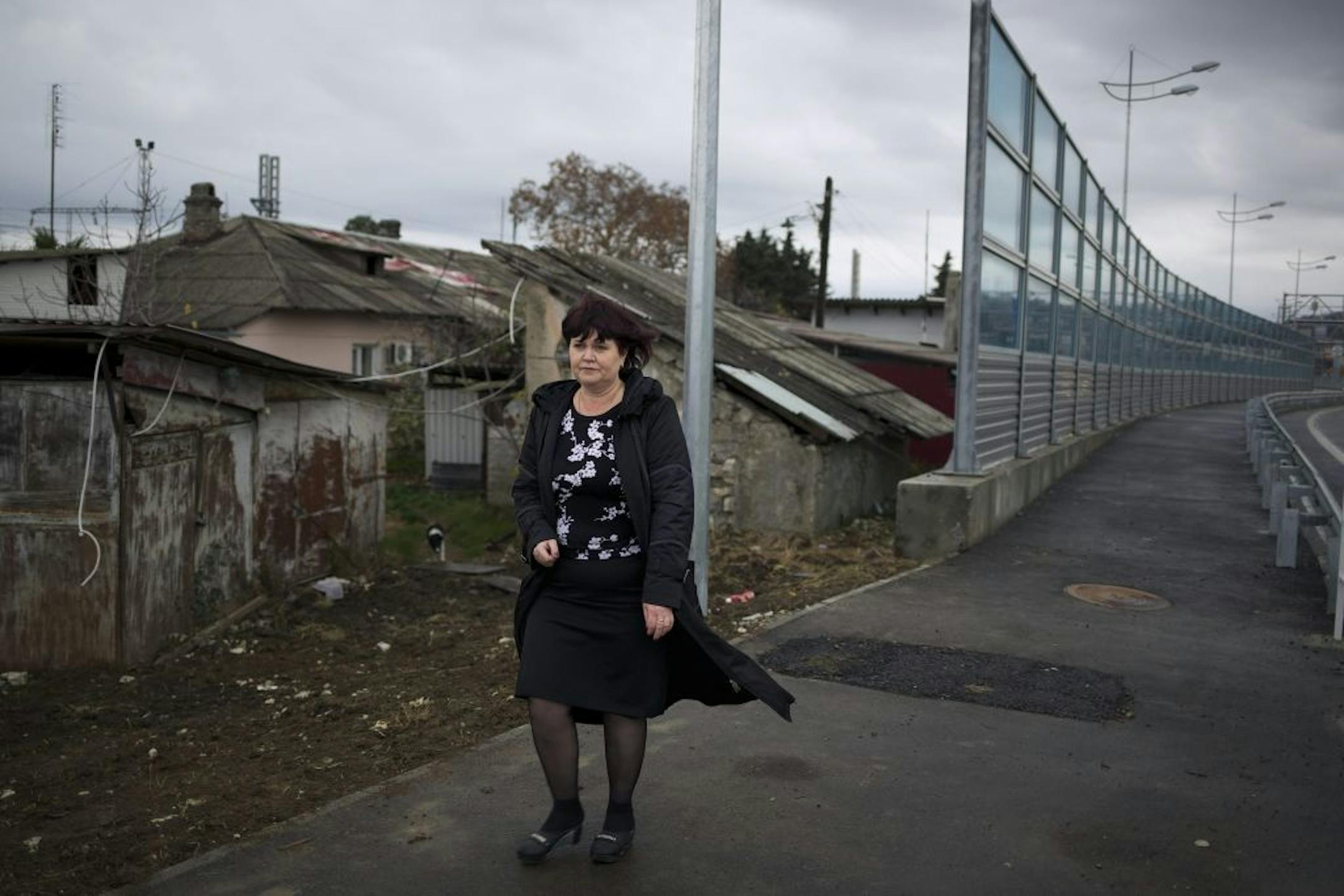 In this photo taken on Wednesday, Nov. 27, 2013, Irina Kharchenko walks away from her house beside the screen separating her yard and a federal highway in the village Vesyoloye outside Sochi, Russia.