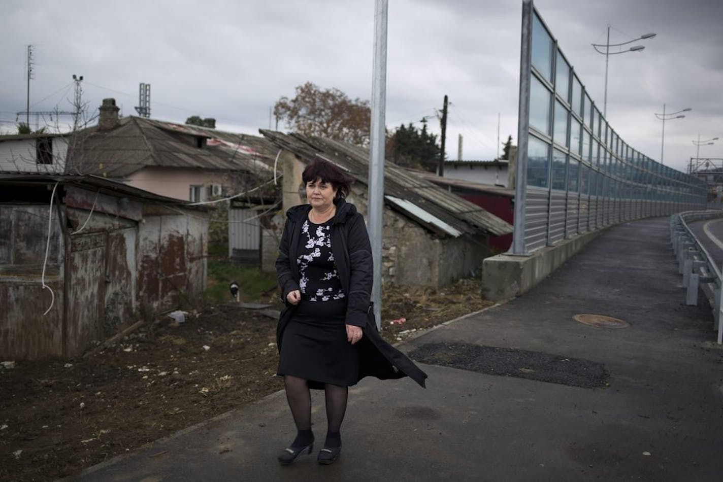 In this photo taken on Wednesday, Nov. 27, 2013, Irina Kharchenko walks away from her house beside the screen separating her yard and a federal highway in the village Vesyoloye outside Sochi, Russia.