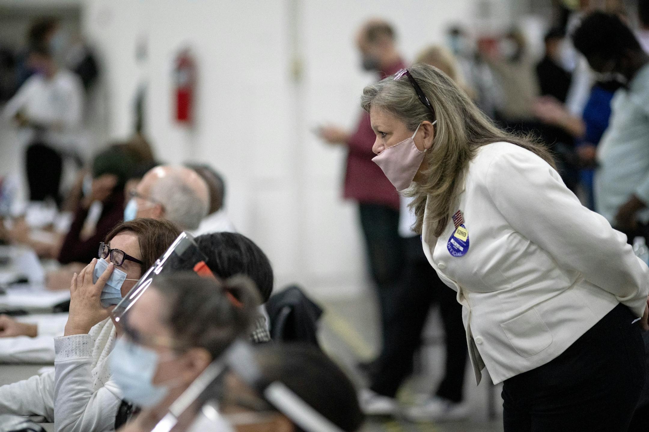 In this Nov. 4, 2020, photo, a Republican election challenger at right watched over election inspectors as they examined a ballot as votes were counted into the early morning hours at the central counting board in Detroit.