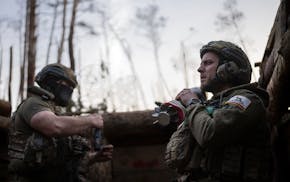 A Ukrainian serviceman from the Azov brigade known by call sign Chaos, right, carries mortar shell, while he waits for a command to fire, at positions