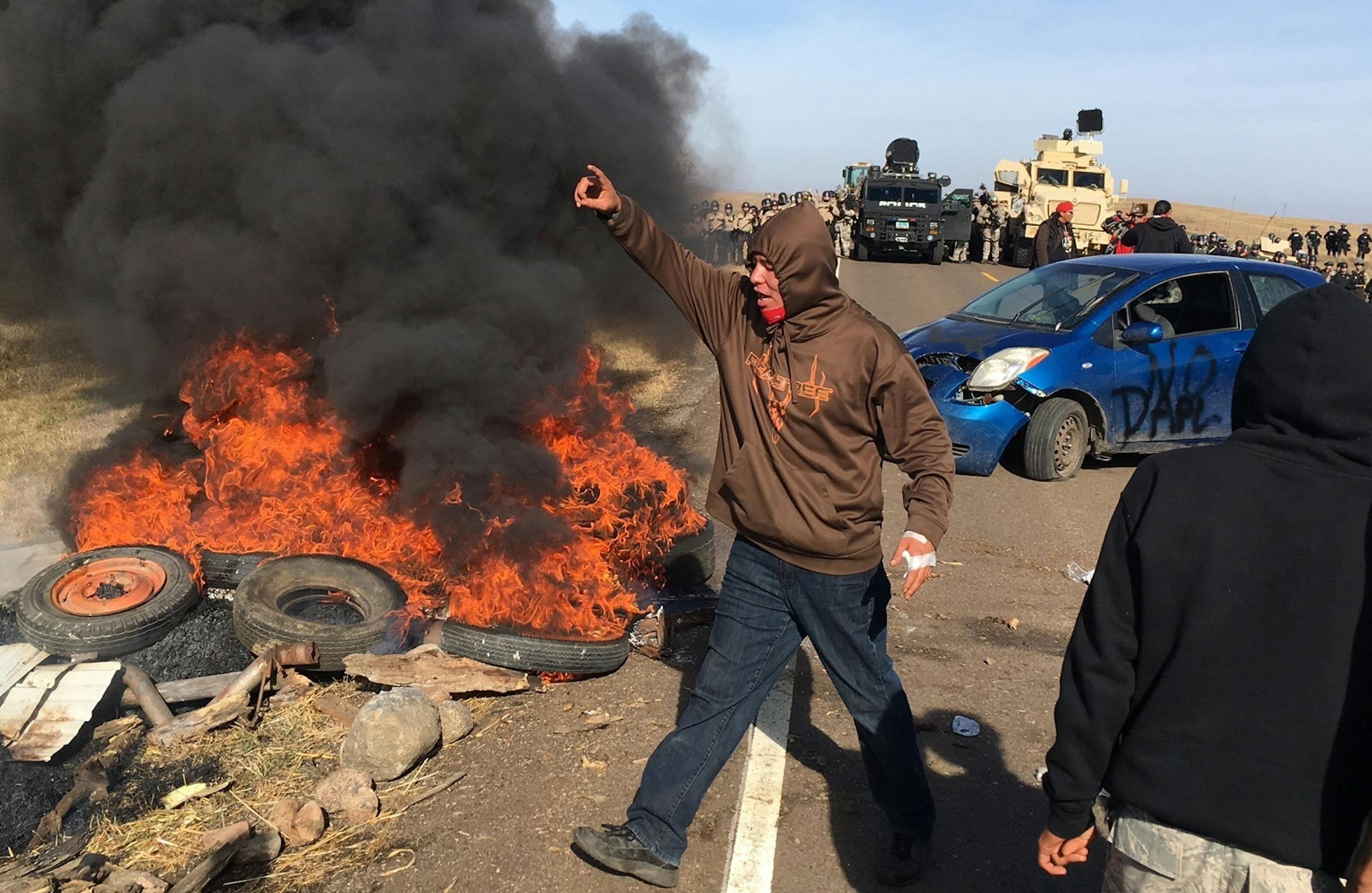 Demonstrators stand next to burning tires as armed soldiers and law enforcement officers assemble on Thursday, Oct. 27, 2016, to force Dakota Access pipeline protesters off private land where they had camped to block construction. The pipeline is to carry oil from western North Dakota through South Dakota and Iowa to an existing pipeline in Patoka, Ill. (Mike McCleary/The Bismarck Tribune via AP) ORG XMIT: MIN2016102715473635
