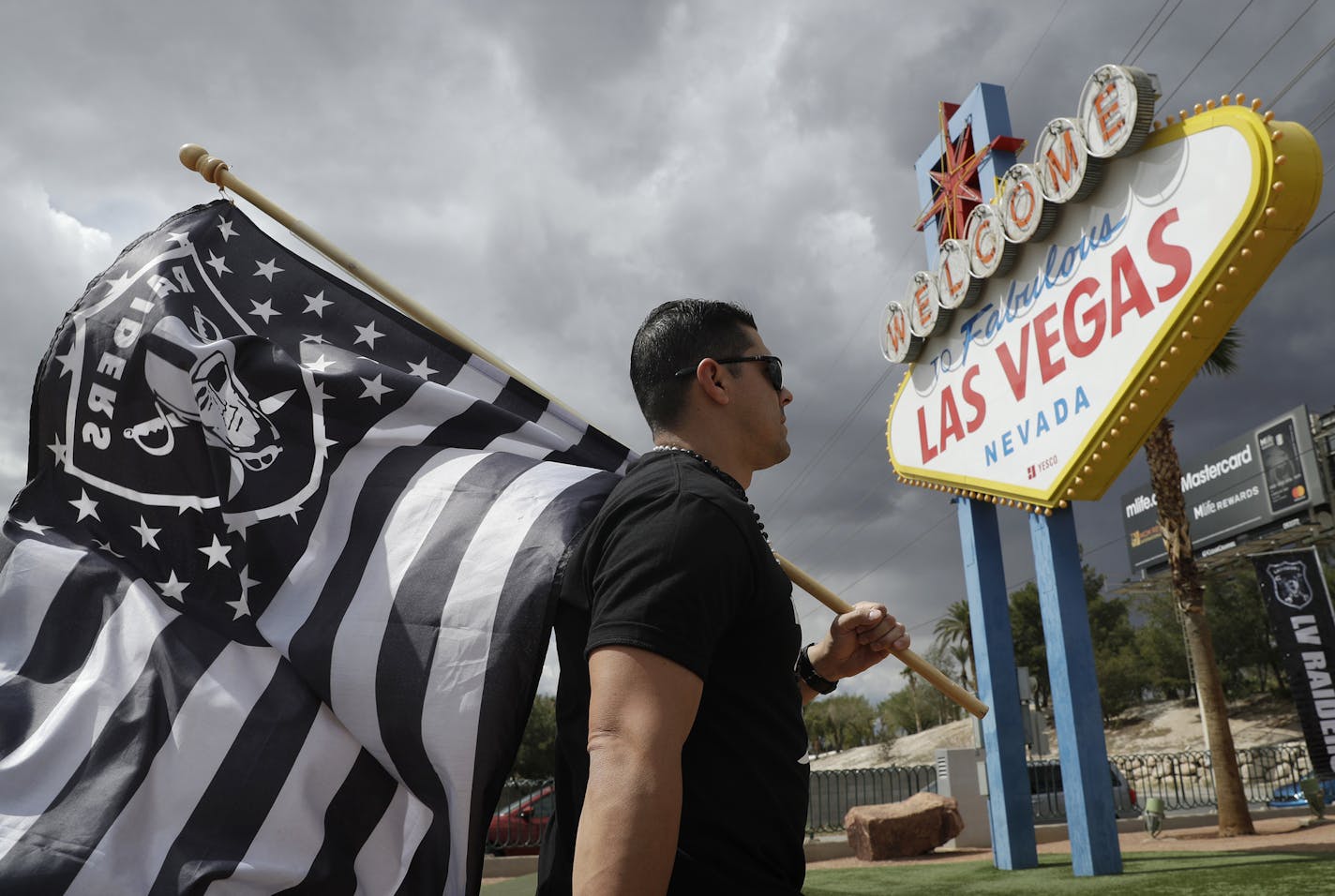 Matt Gutierrez carries a raiders flag by a sign welcoming visitors to Las Vegas, Monday, March 27, 2017, in Las Vegas. NFL team owners approved the move of the Raiders to Las Vegas in a vote at an NFL football annual meeting in Phoenix. (AP Photo/John Locher)