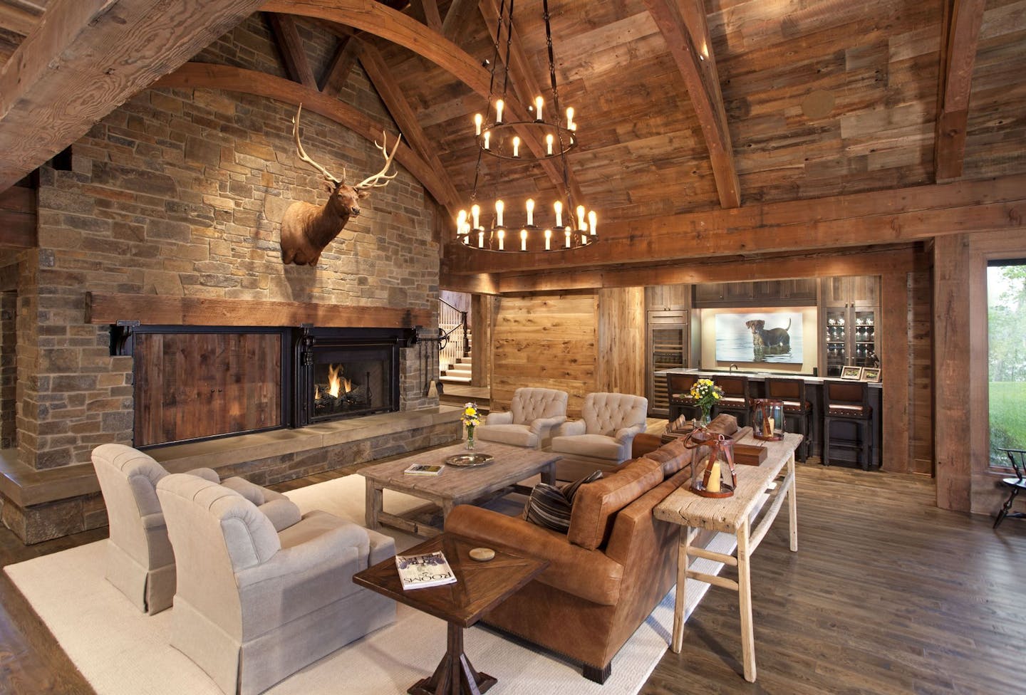 The great room's curved timbers, reclaimed barn wood and Montana stone fireplace. A built-in bar for entertaining is on the far wall.