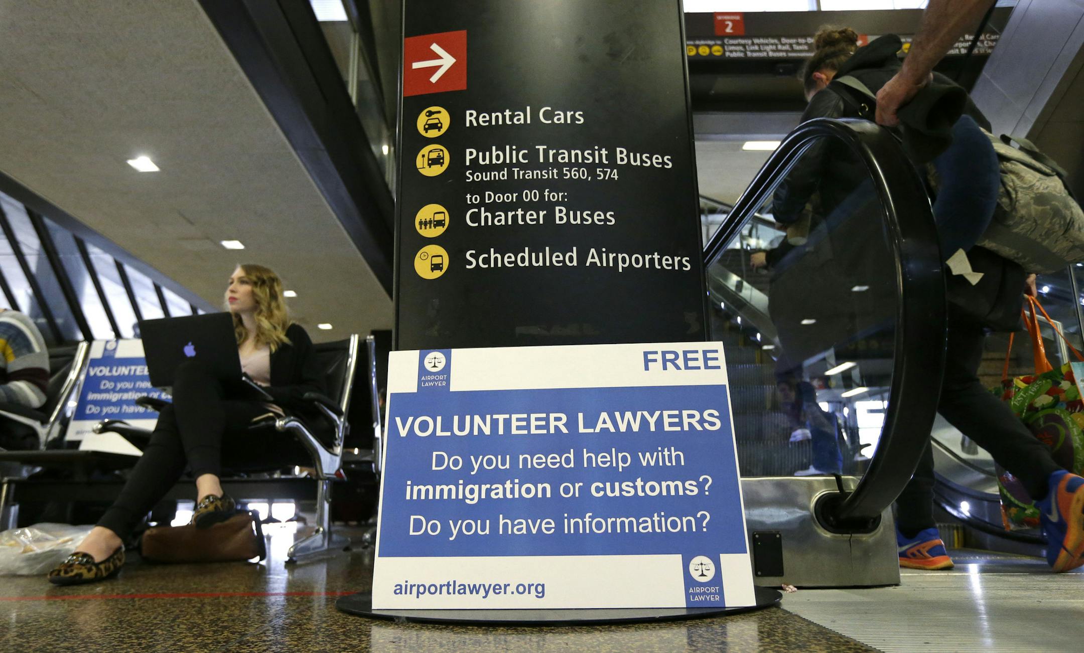 Asti Gallina, left, a volunteer law student from the University of Washington, sits at a station near where passengers arrive on international flights at Seattle-Tacoma International Airport Tuesday, Feb. 28, 2017, in Seattle. Gallina was volunteering with the group Airport Lawyer, which also offers a secure website and mobile phone app that alerts volunteer lawyers to ensure travelers make it through customs without trouble. Airport officials and civil rights lawyers around the country are gett
