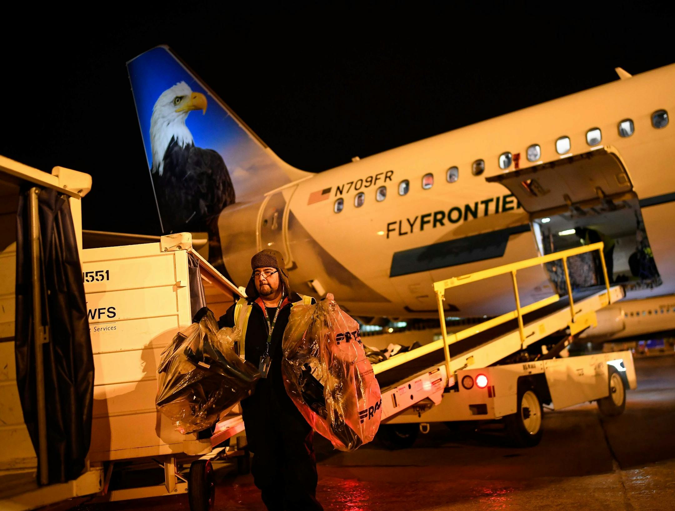 A Frontier Airlines baggage handler worked to unload luggage from an inbound jet from Denver, which arrived after 1 a.m. Friday.
