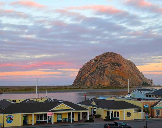 Morro Rock on the Central Coast of California stands silhouetted against the reflected colors of the dawn sky.
