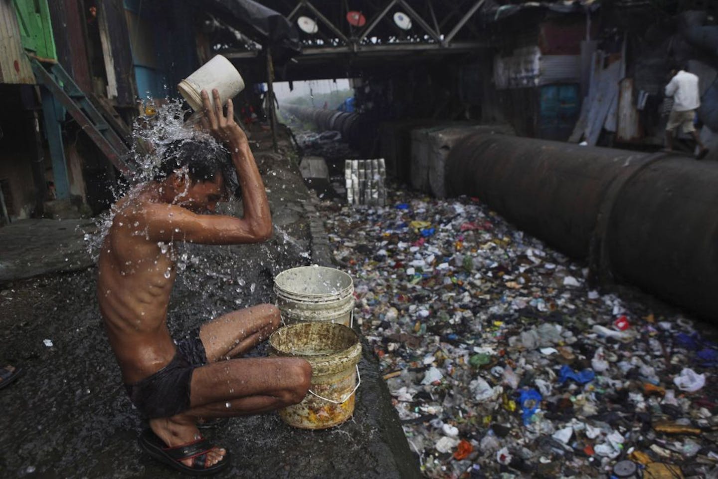 A migrant worker bathing near an open sewer at a slum in Mumbai, India.