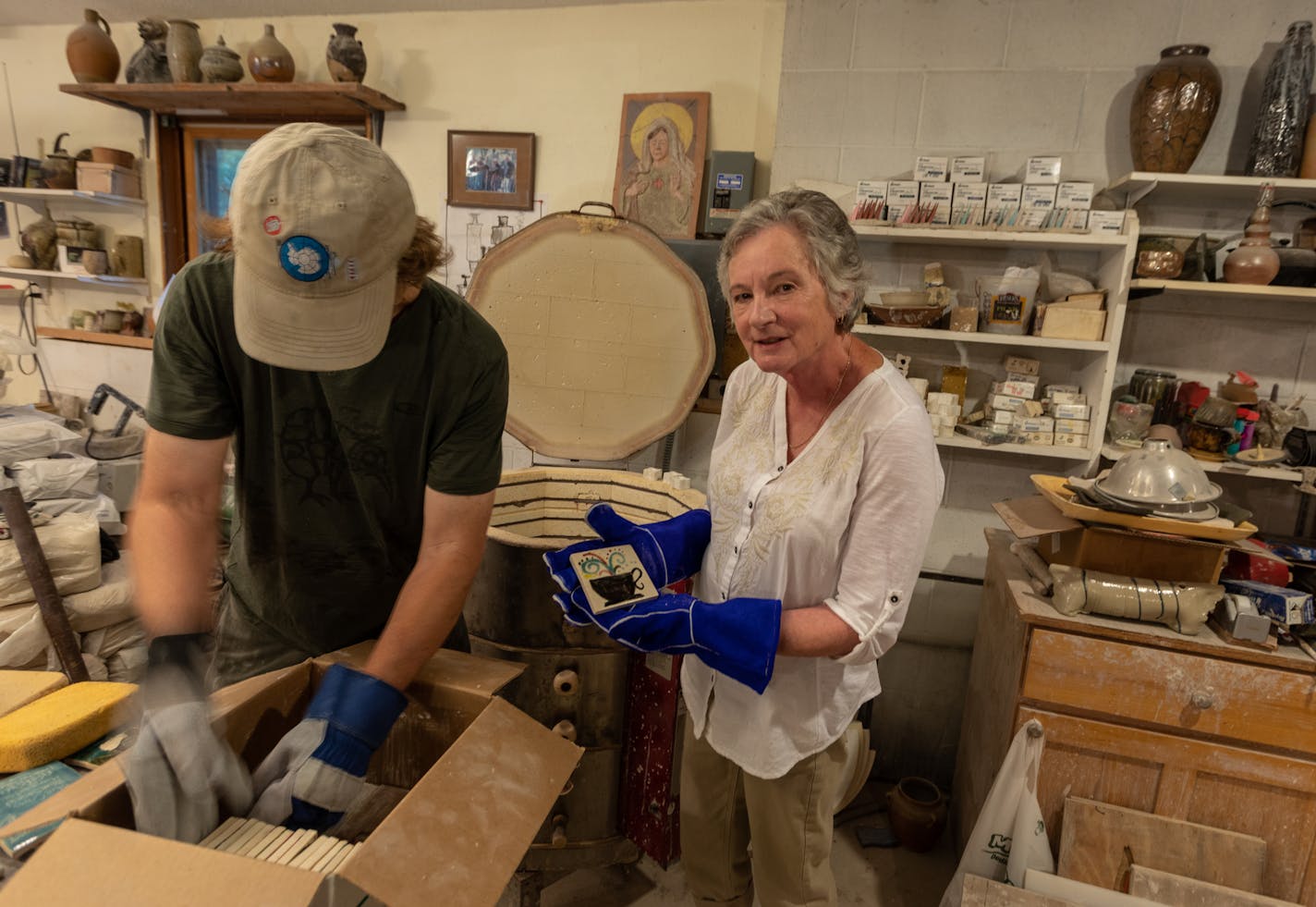 New London potter Bill Gossman, left, and Janet Olney, executive director of the Willmar Area Arts Council, pull newly fired tiles from his kiln. The tiles are among 600 that have been painted by community members for installation on eight benches around Willmar as part of a public art project.