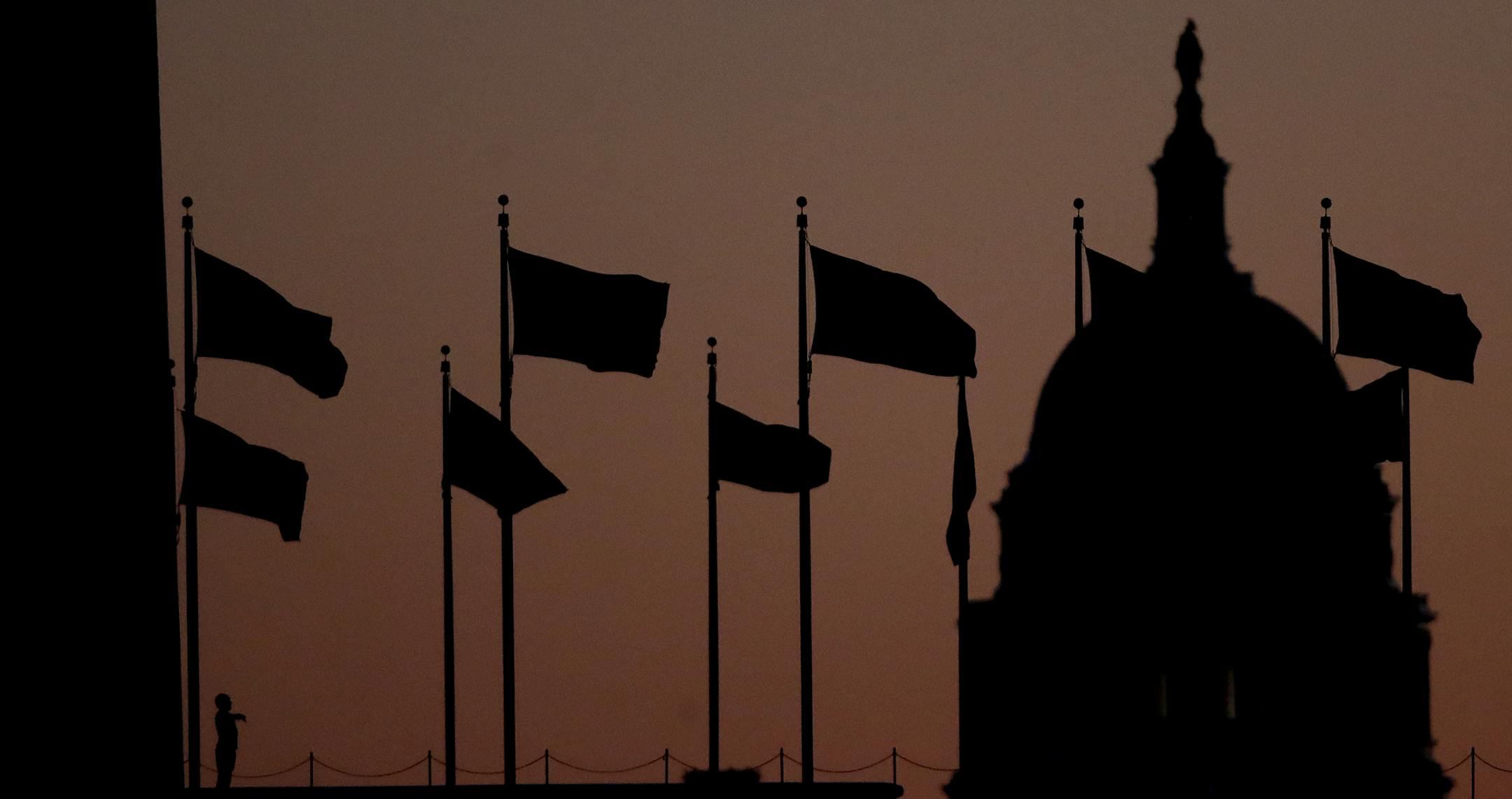 A person, left, stands at the base of the Washington Monument, left, as the U.S. Capitol building gives backdrops to U.S. flags before sunrise on Capitol Hill in Washington, Thursday, Dec. 19, 2019, a day after the U.S. House voted to impeach President Donald Trump on two charges, abuse of power and obstructing Congress. (AP Photo/Julio Cortez)