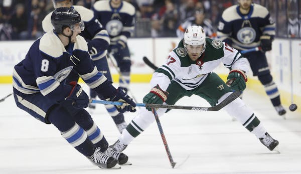 Columbus Blue Jackets' Zach Werenski, right, knocks the puck away from Minnesota Wild's Marcus Foligno during the first period of an NHL hockey game T