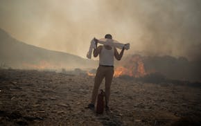 A man wraps his shirt over his face as he tries to extinguish a fire, near the seaside resort of Lindos, on the Aegean Sea island of Rhodes, southeast