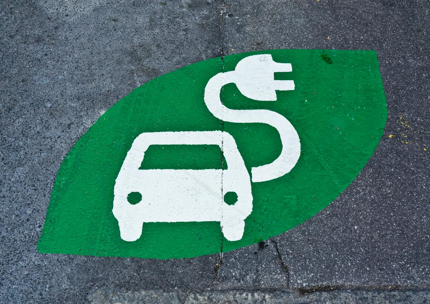 Electric car sign, charging station, green sign painted on street. Electric vehicle sign with car and plug, uploading place.