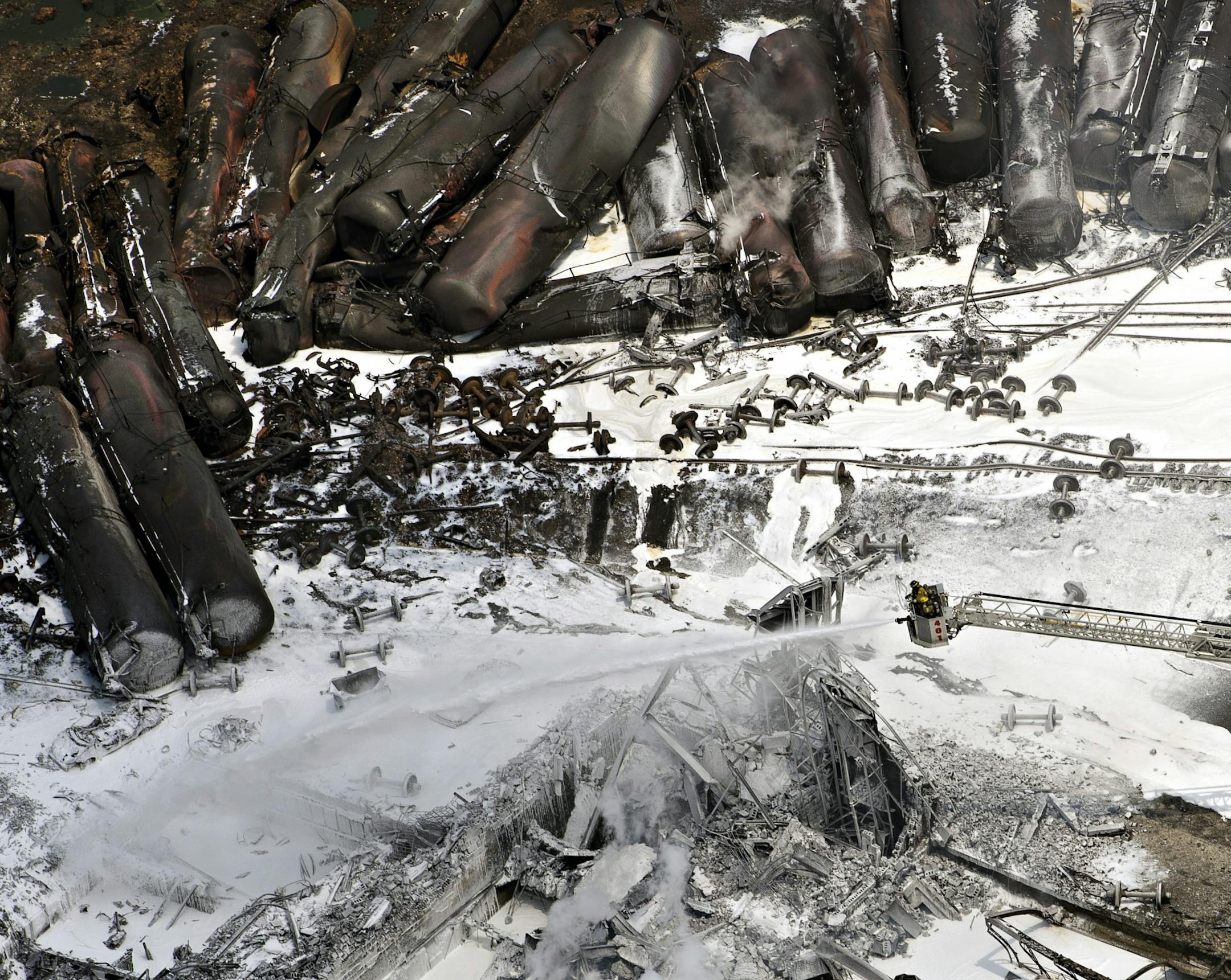 Fire fighters continue to water smoldering rubble Sunday, July 7, 2013 in Lac Megantic, Quebec. A runaway train derailed Saturday igniting tanker cars carrying crude oil.