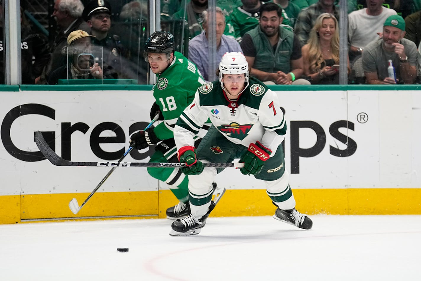 Minnesota Wild defenseman Brock Faber (7) moves to take control of the puck in front of Dallas Stars center Max Domi (18) during Game 2 of an NHL hockey Stanley Cup first-round playoff series, Wednesday, April 19, 2023, in Dallas. (AP Photo/Tony Gutierrez)