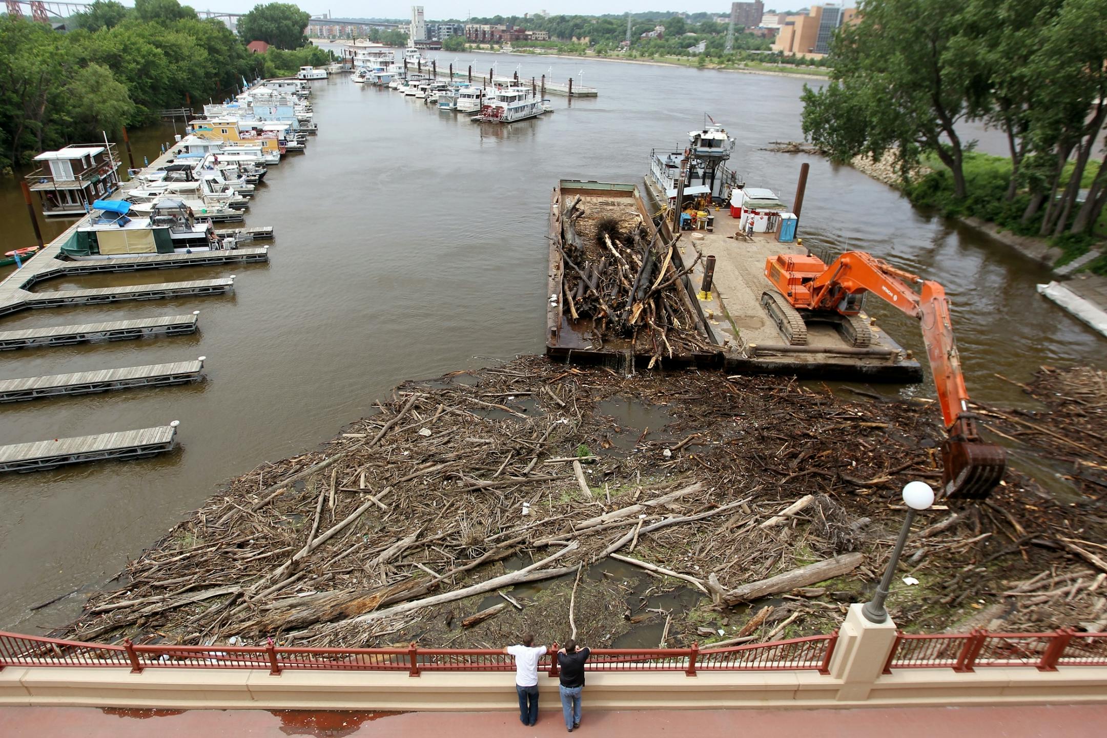 Logs and debris are lifted by a back-hoe to clear a log jam in the Mississippi River near the Wabasha St. Bridge in St. Paul, Minn., on Friday, July 5, 2013.