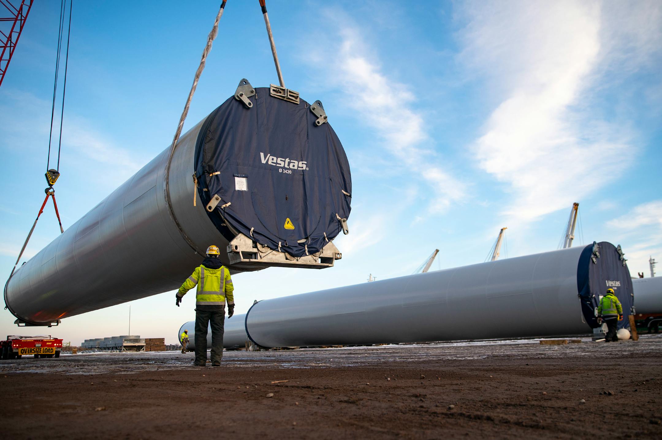 A crane lowered a section of wind turbine tower from a flatbed truck and onto a storage field.