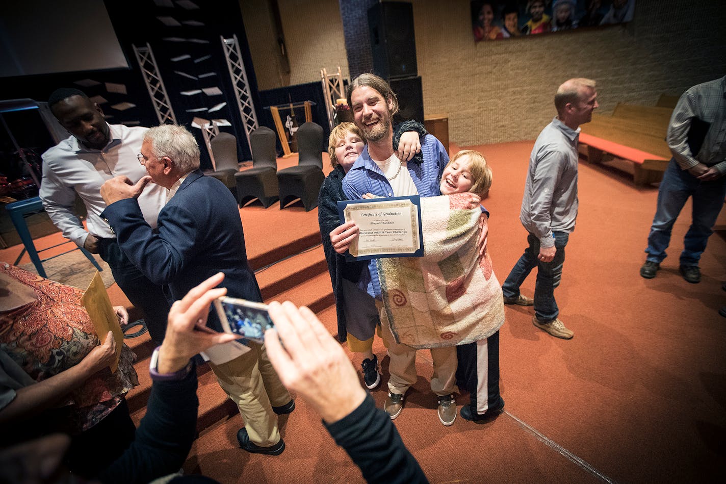 Alex Farchmin celebrated with his sons, Eian, 13, left, and Owen, 11, after he graduated from the Minnesota Adult & Teen Challenge treatment program in Minneapolis. The boys often wrap themselves in blankets that once belonged to their dad and mom, who died in August, to help them feel secure.