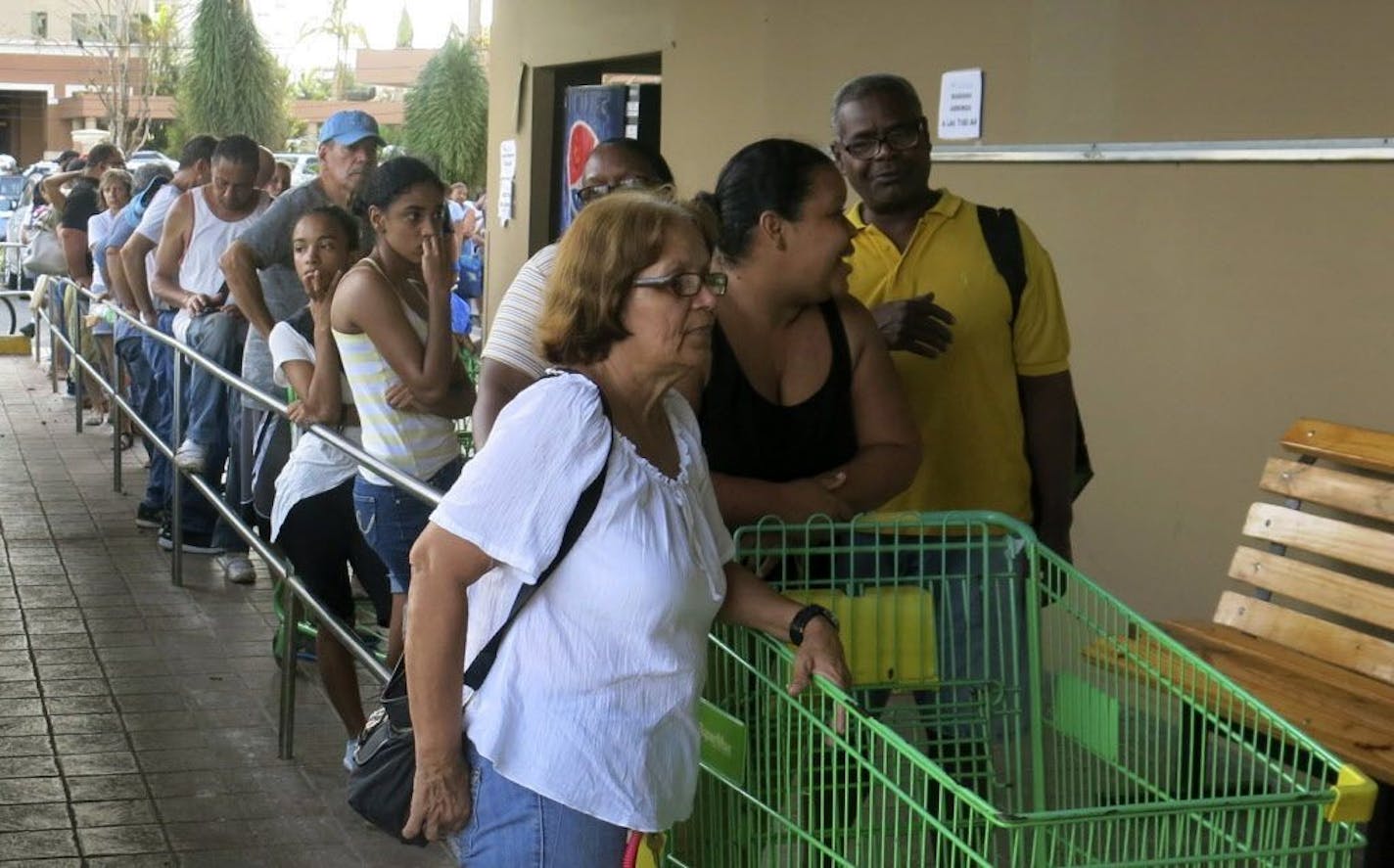 FILE - In this Sept. 25, 2017, file photo, people wait in line outside a San Juan grocery store to buy food after Hurricane Maria.