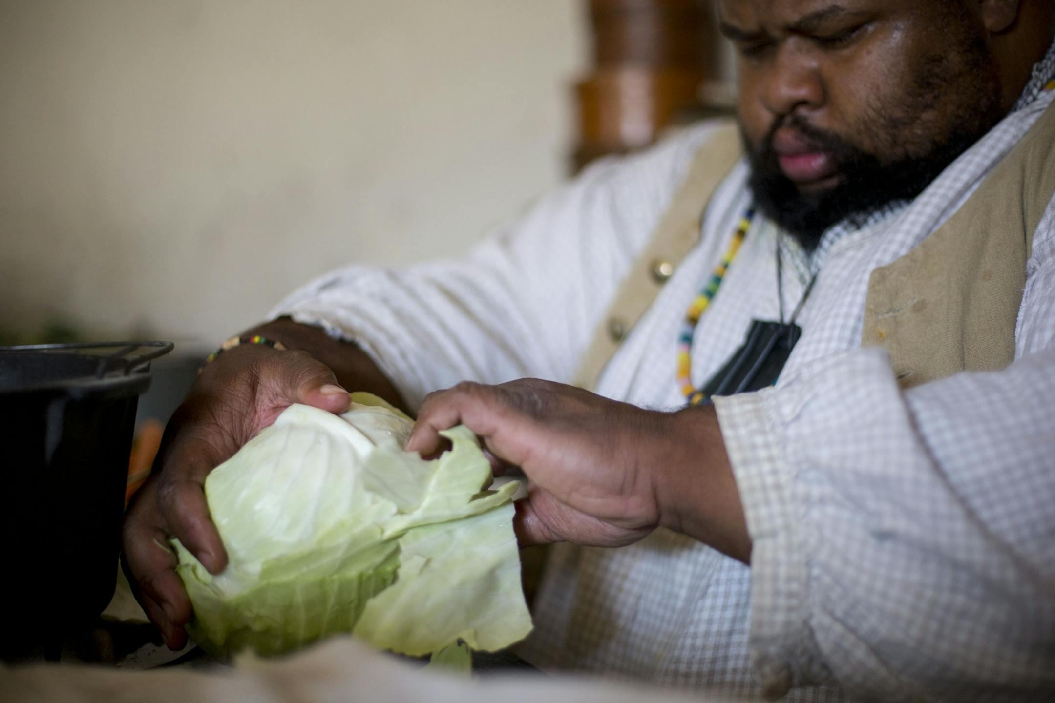 Michael Twitty peels leaves of cabbage to line the kettle before he places the chicken in it.