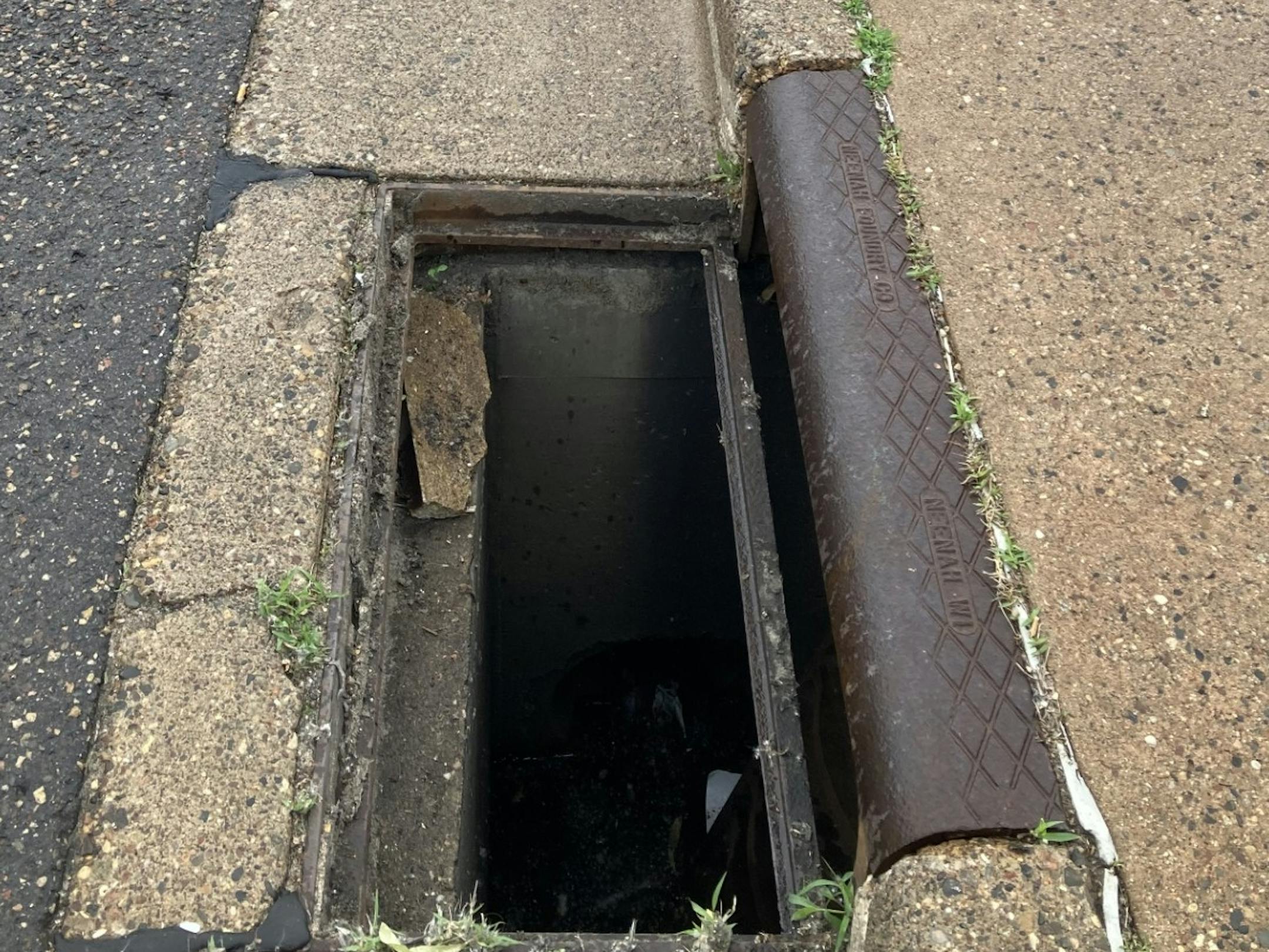 A photograph of a concrete gutter in a street, with three long rectangular openings where storm drain covers should be.