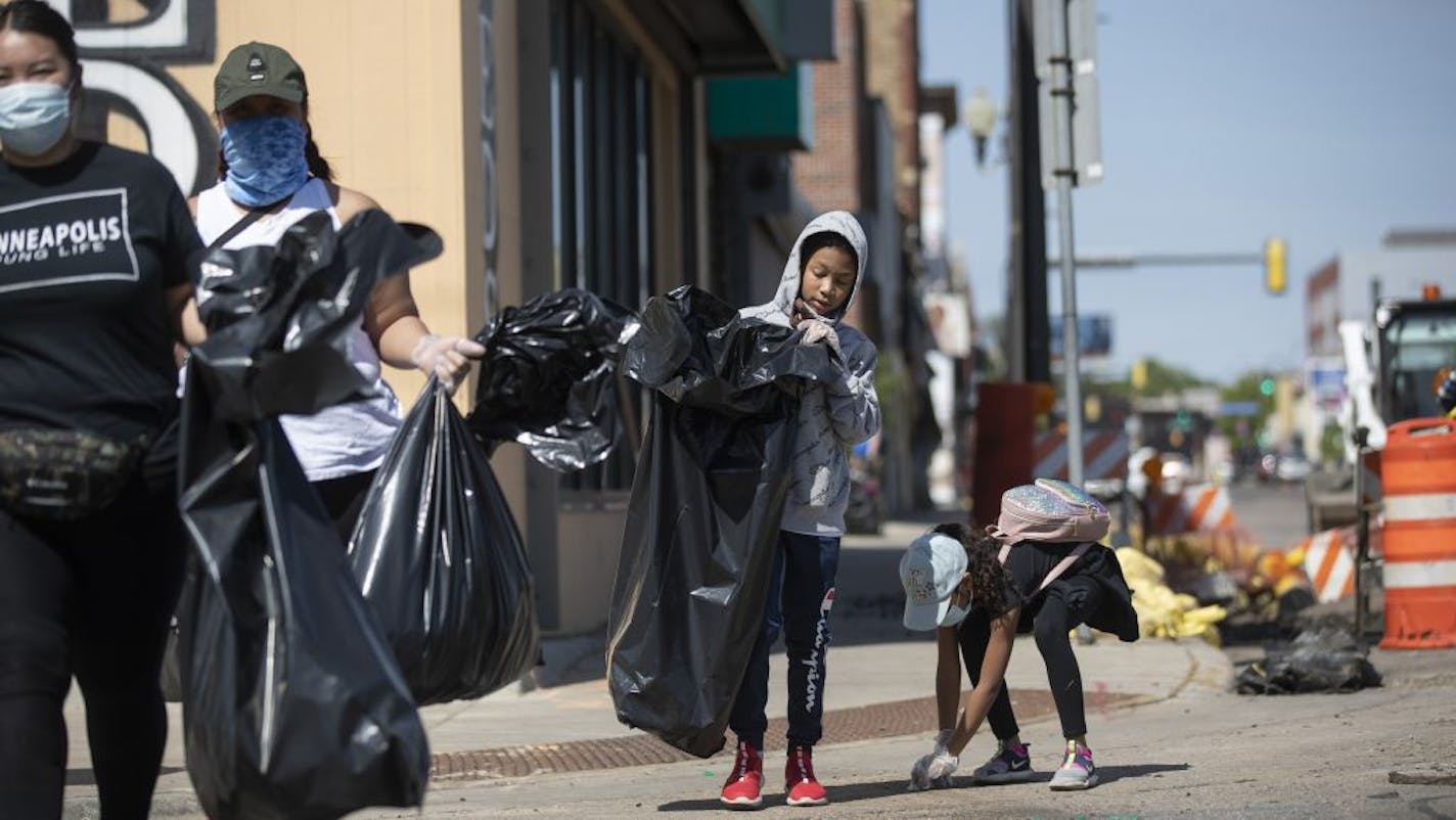 Aideyn Souvannarath, 13, picks up trash and debris left from recent damage to stores along West Broadway in north Minneapolis, Sunday May 31, 2020, after days of protests over the death of George Floyd.