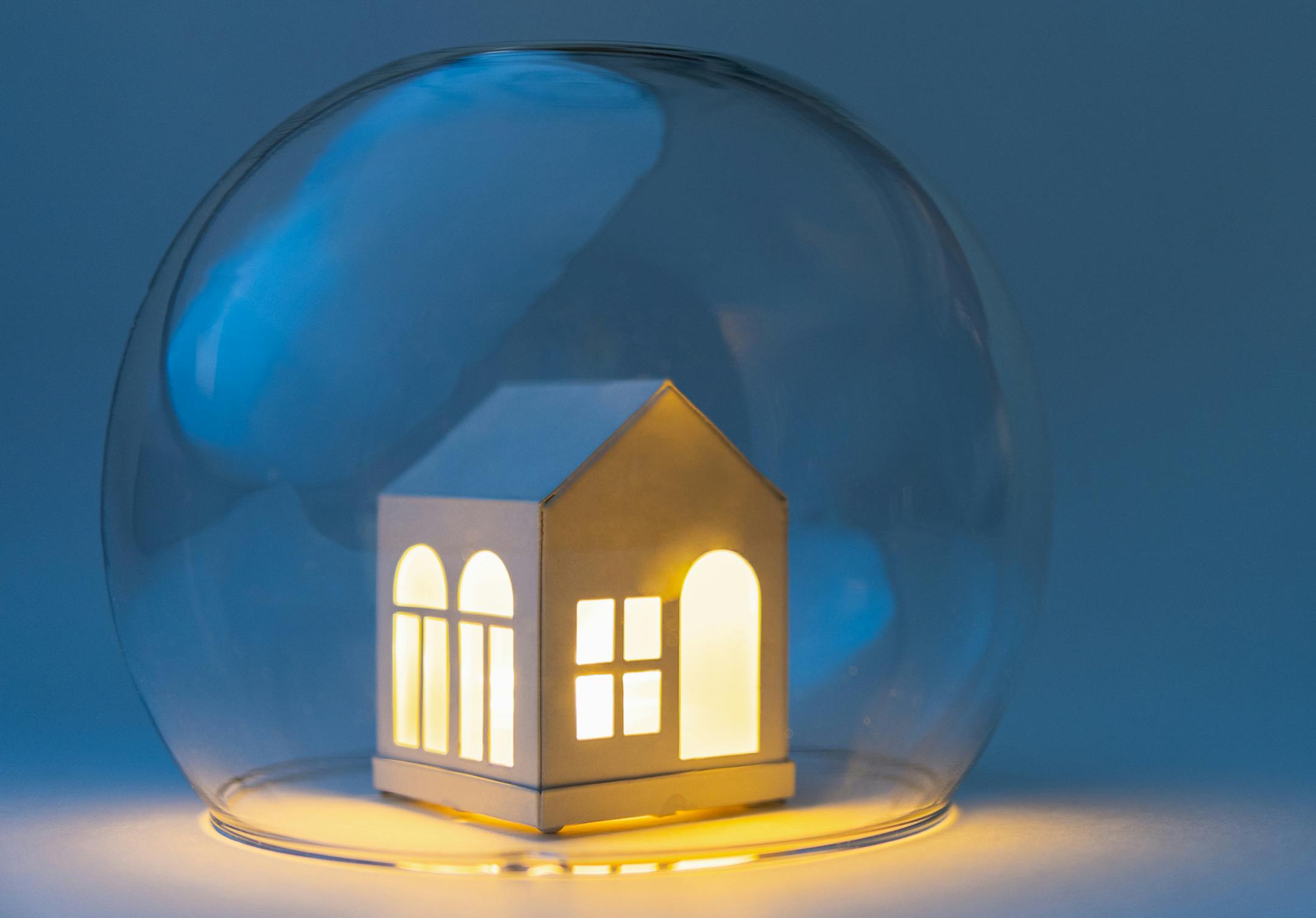 Conceptual image of safety when staying at home during Corona virus COVID-19 quarantine lockdown. Toy house protected by glass bowl.