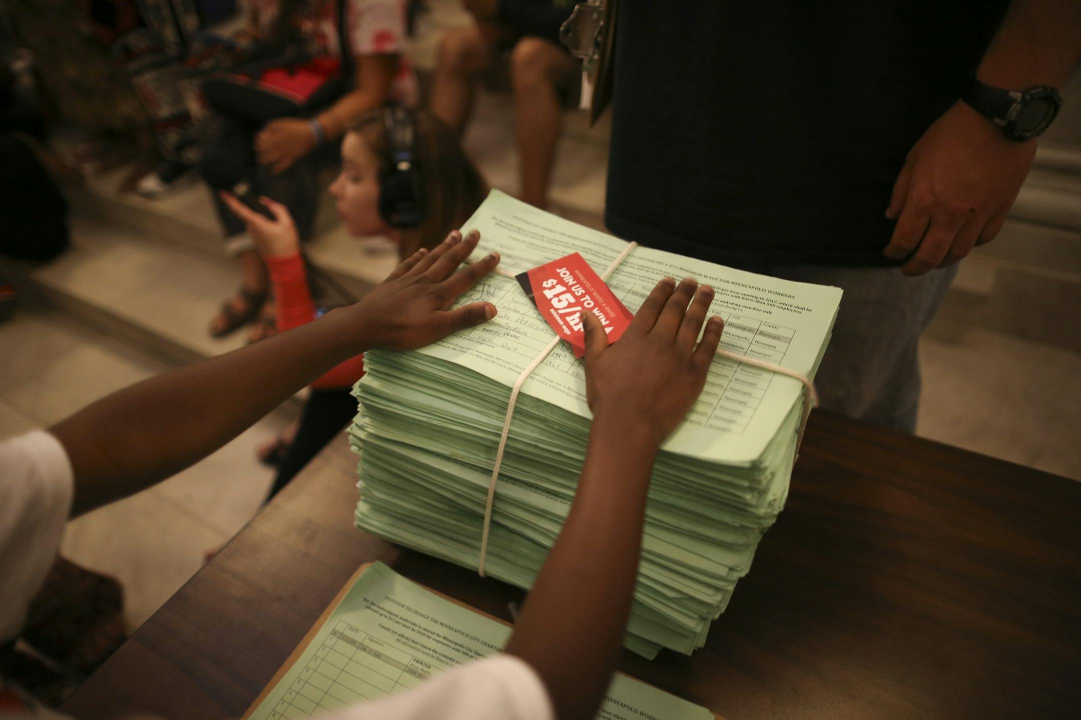 A young man put his hands on the stack of signed petitions in support of a $15 minimum wage as demonstrators rallied in City Hall and heard speeches before handing over a petition with 20,000 signatures on it to the City Clerk.