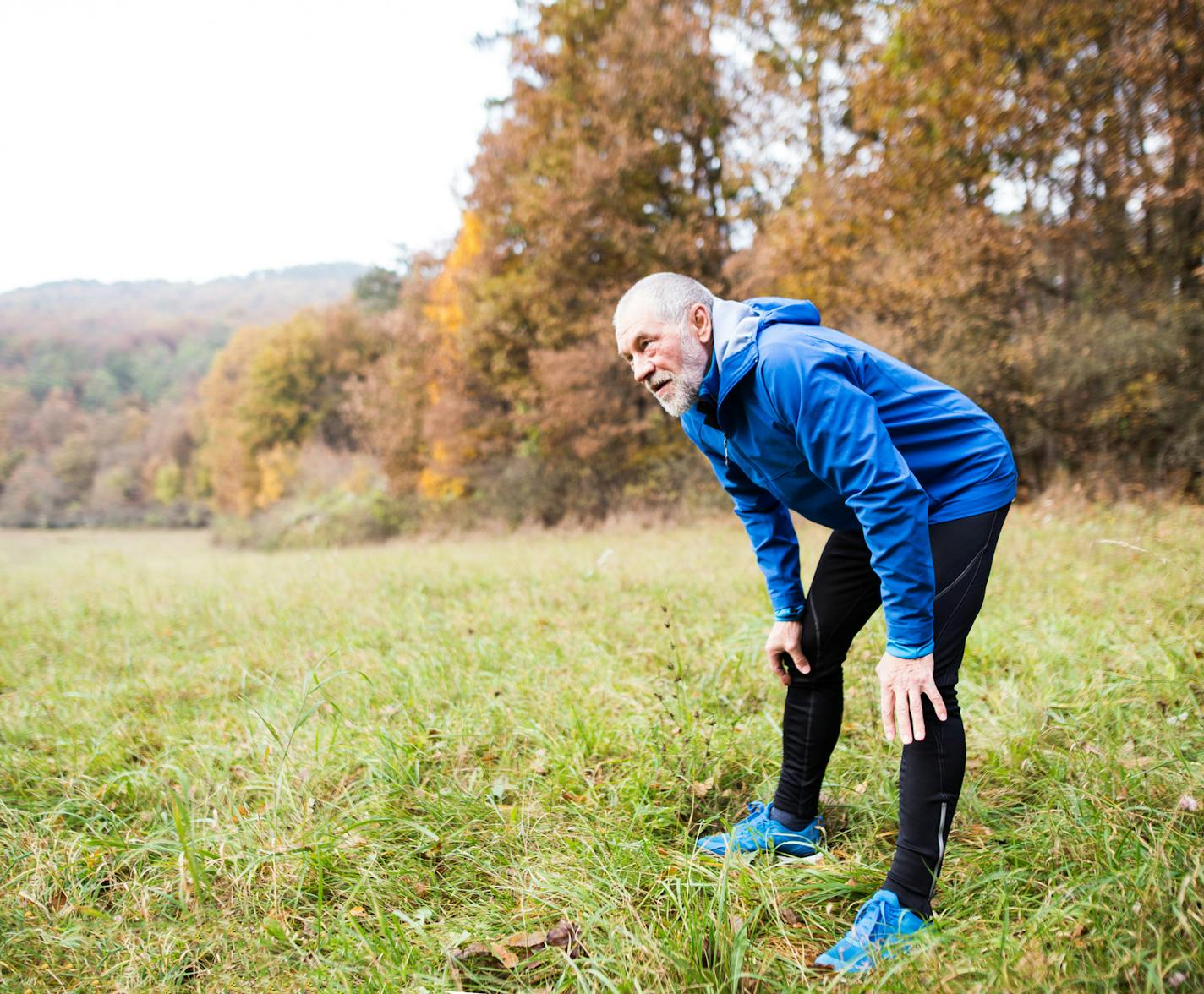 Senior runner in blue jacket resting outside in sunny autumn nature. istock