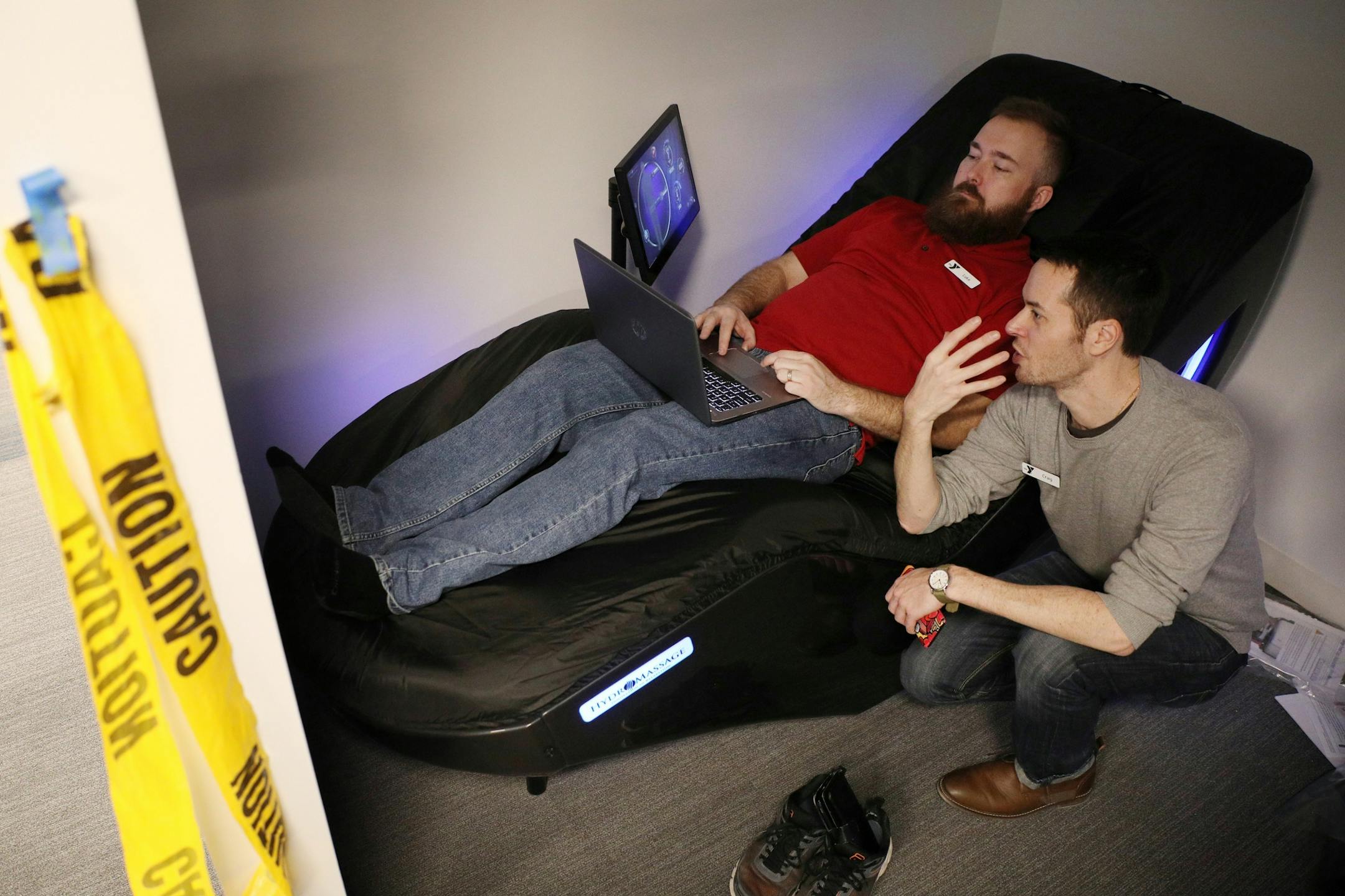 YMCA employees Luke Baker, left, and Craig Paulnock talked as Baker sat on a hydromassage chair.