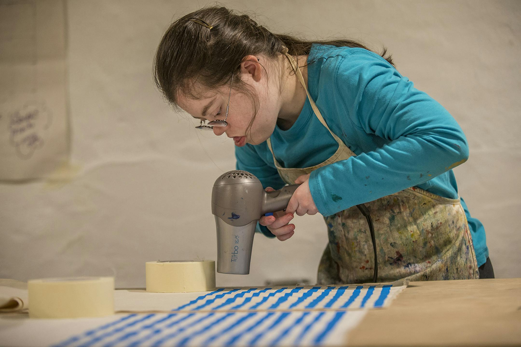 Julia Tyler uses a hair dryer to dry the paint on her silk screened placemats as she works in the basement of the Compendium Boutique in Swarthmore and creates textiles for her company, Dance Happy Designs. (Michael Bryant/Philadelphia Inquirer/TNS) ORG XMIT: 1540254 ORG XMIT: MIN2001140333341160