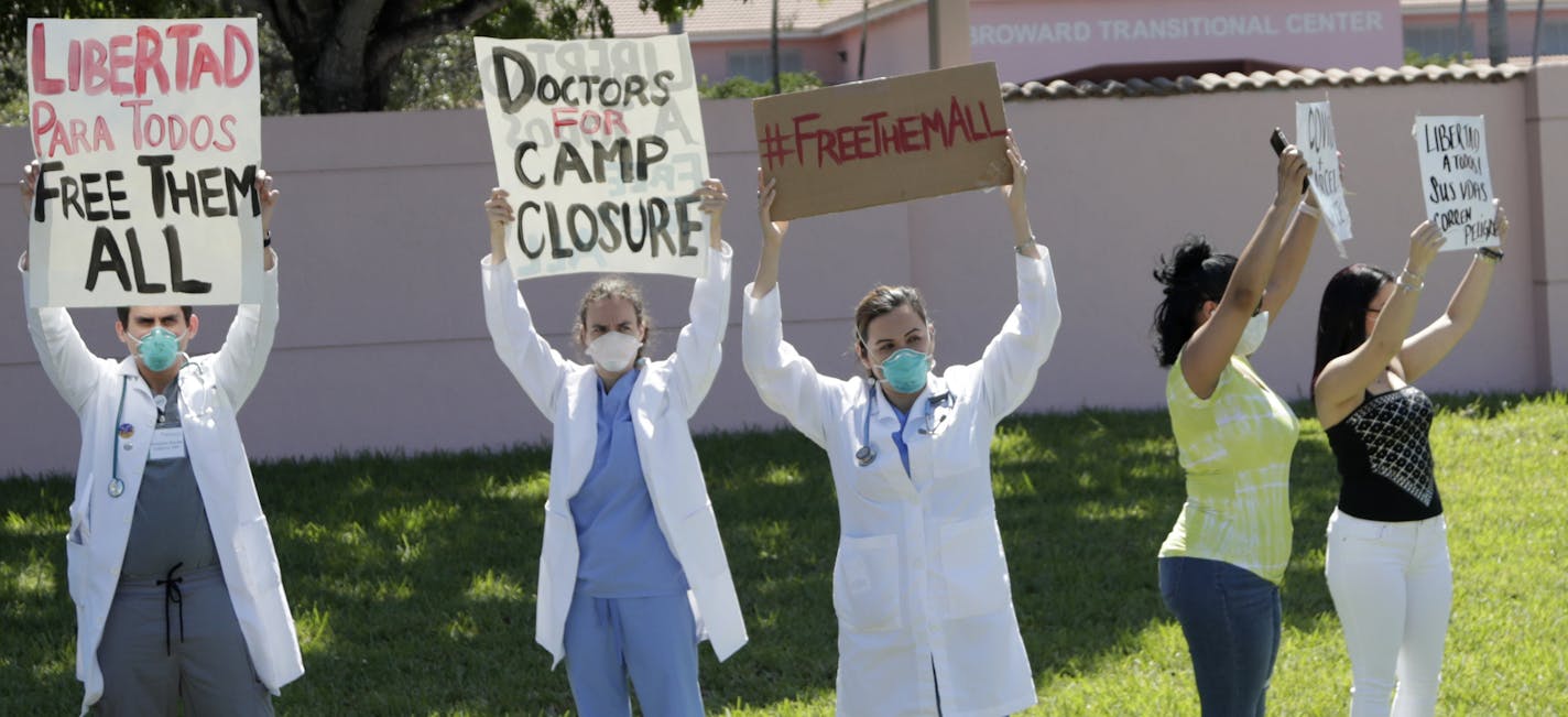 Dr. Franklyn Rocha Cabrero, left, and Dr. Claudia Alvarez, center, and others protest conditions that detainees being held by Immigration and Customs Enforcement face outside of the Broward Transitional Center, during the new coronavirus pandemic, Friday, May 1, 2020, in Pompano Beach, Fla. A Miami federal judge has ordered the release of some detainees from ICE custody at three South Florida detention centers due to conditions related to COVID-19. (AP Photo/Lynne Sladky)