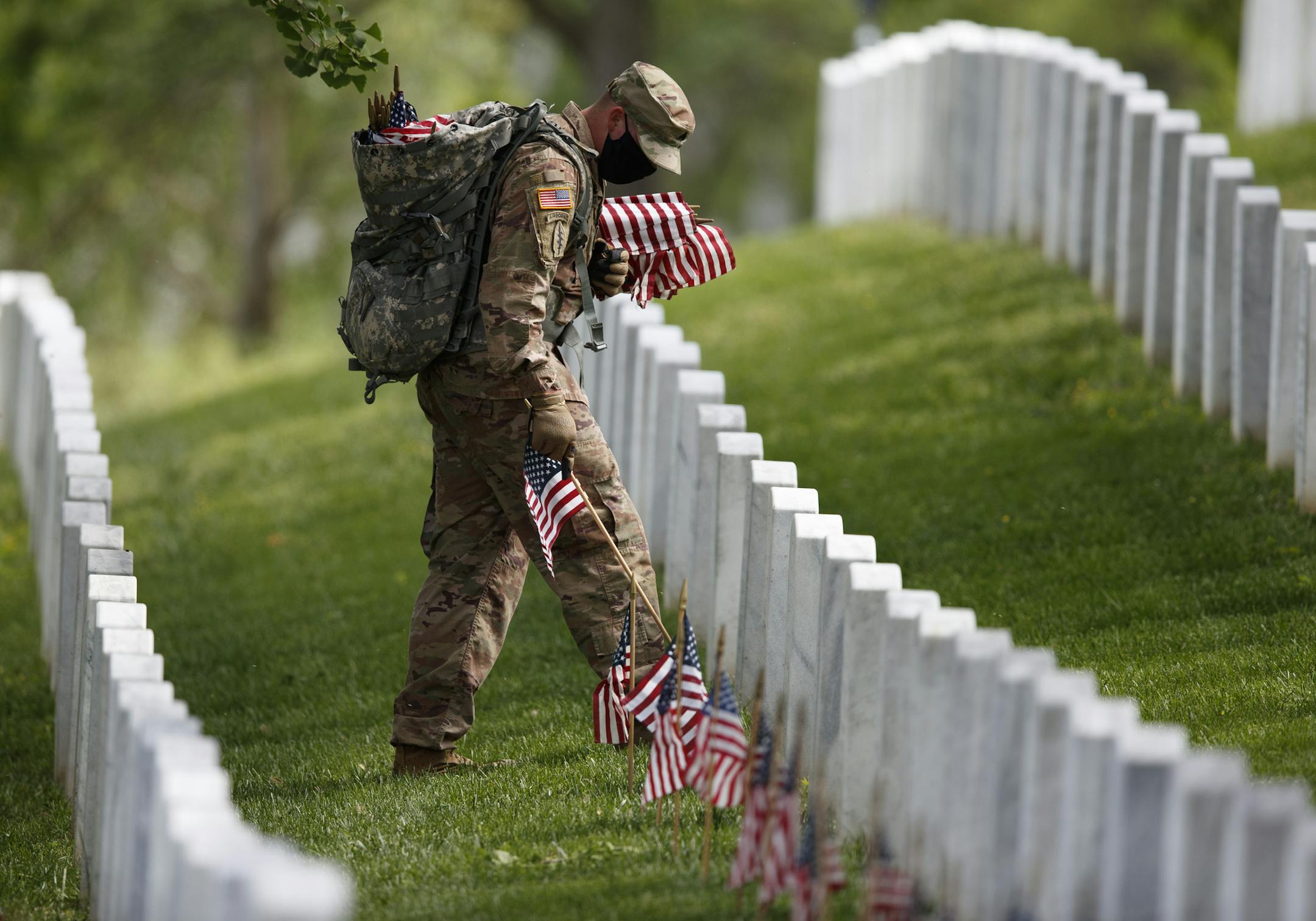 A member of the 3rd U.S. Infantry Regiment also known as The Old Guard, wears a face mask as he places flags in front of each headstone for "Flags-In" at Arlington National Cemetery in Arlington, Va., Thursday, May 21, 2020, to honor the Nation's fallen military heroes ahead of Memorial Day. (AP Photo/Carolyn Kaster)
