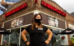 Claudia Gutierrez Mendez wearing black T-shirt and black face mask standing outside Hamburguesas El Gordo restaurant in Minneapolis with her hands on 