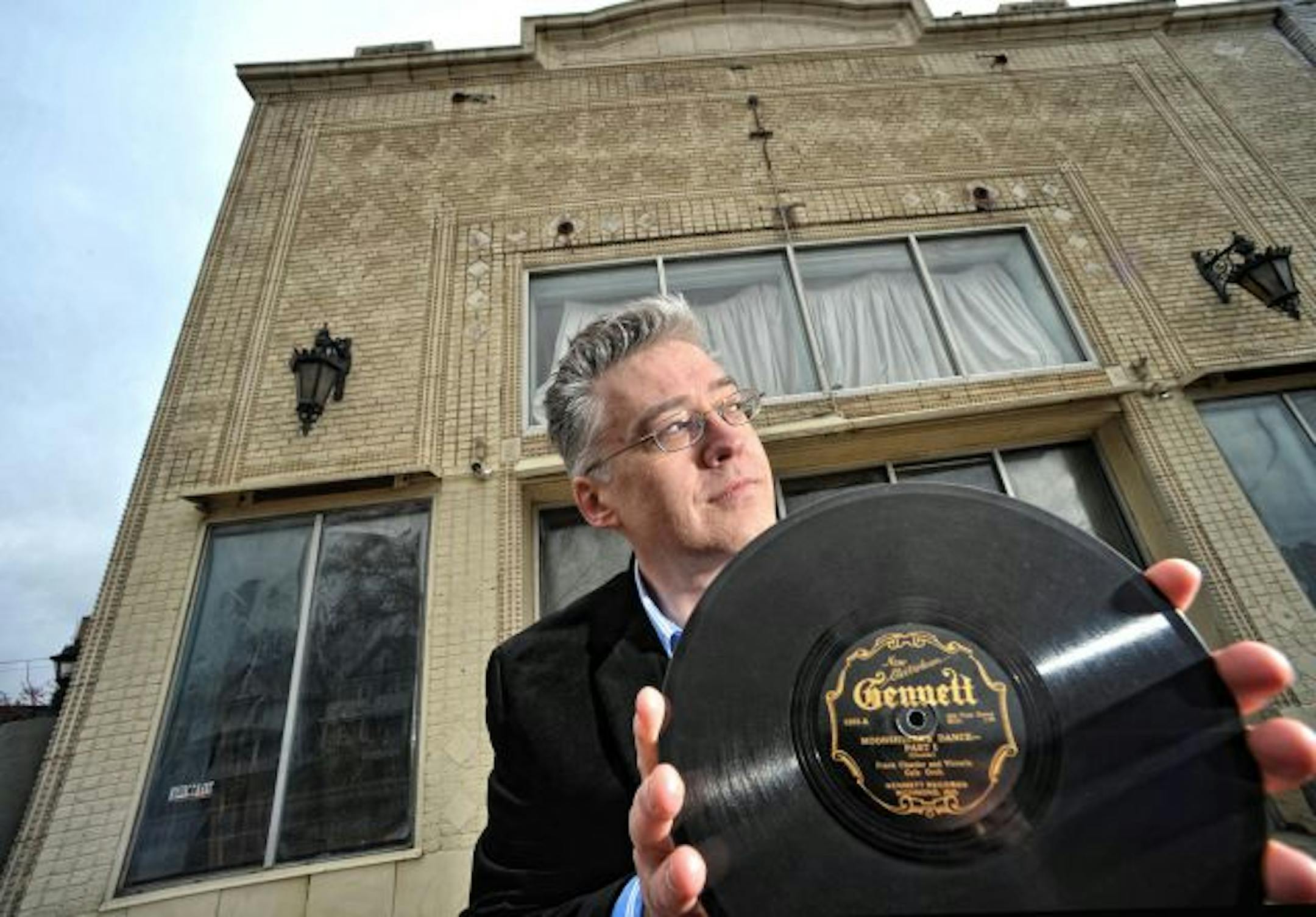 Kurt Gegenhuber held an original 78 rpm record of "Moonshiner's Dance Part One" by Frank Cloutier and the Victoria Cafe Orchestra, part of the Anthology of American Folk Music. He recently discovered the building behind him is the Victoria Theater on University Avenue in St. Paul where the band played. Thi discovery is part of a campaign to save the building.