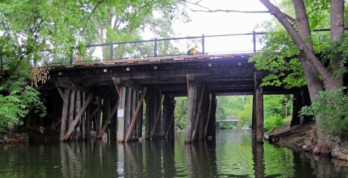 Existing wooden railroad bridge: The bridge has six rows of wooden piers. Each side has different types of railing. View is looking west with the Burnham Road Bridge in the background.