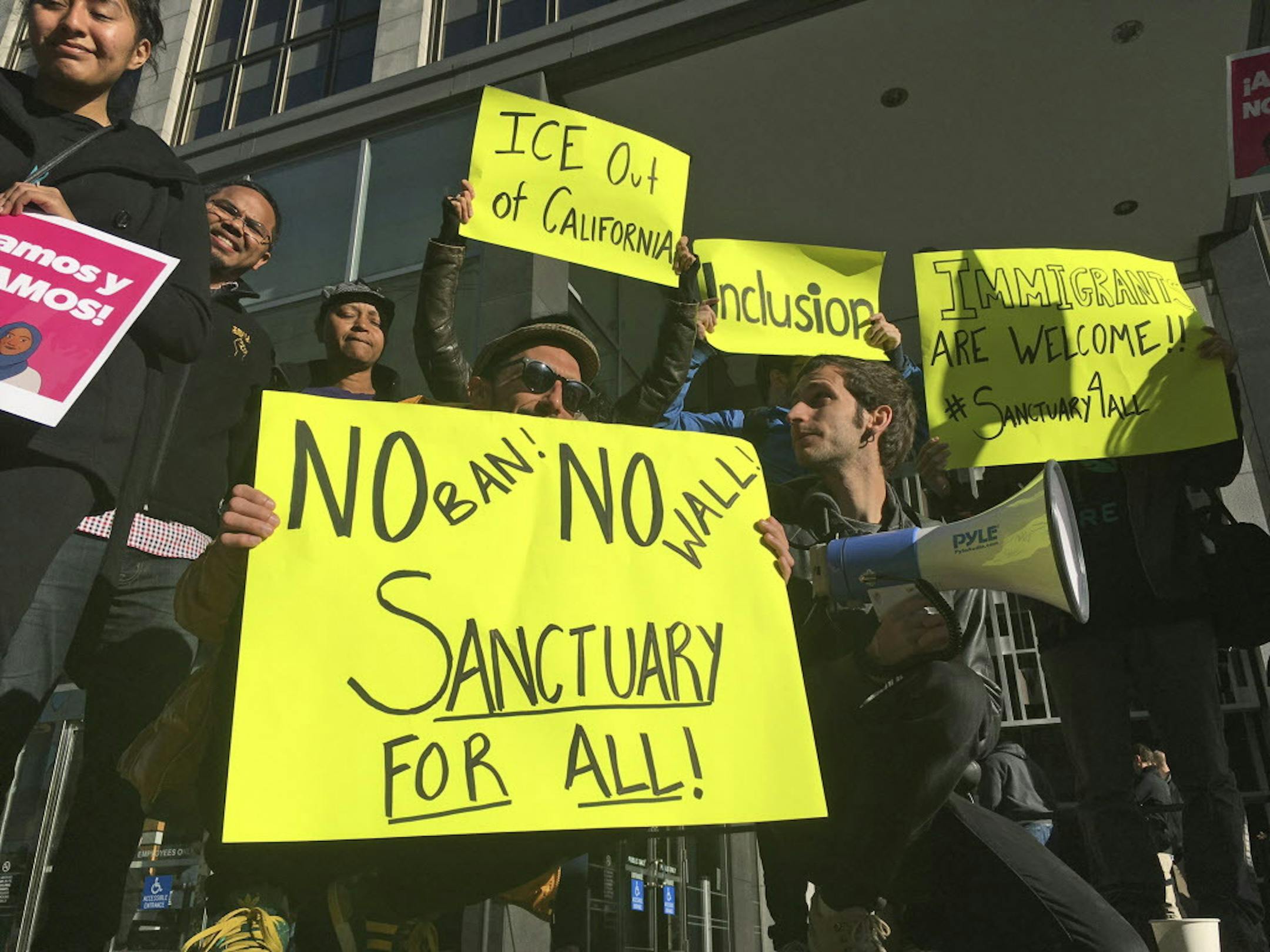 Protesters hold up signs outside a courthouse where a federal judge will hear arguments in the first lawsuit challenging President Donald Trump's executive order to withhold funding from communities that limit cooperation with immigration authorities Friday, April 14, 2017, in San Francisco. U.S. District Court Judge William Orrick has scheduled a hearing on Friday on San Francisco's request for a court order blocking the Trump administration from cutting off funds to any of the nation's so-call