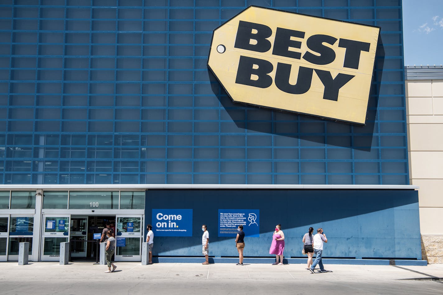 Socially distanced people wearing face masks, wait in line outside a Best Buy electronics store at The Fountains at Farah shopping complex in El Paso, Texas on Tuesday July 7, 2020.