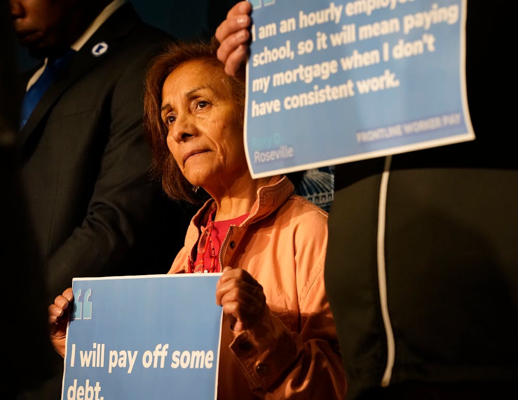 Frontline workers held up signs, including Sylvia Martinez, left, and Bill Schwandt, during a news conference announcing Frontline Worker Pay.